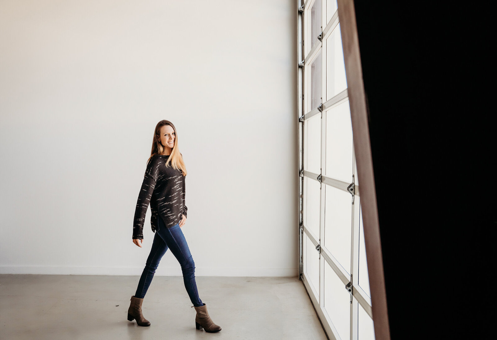 Branding Photographer,  a woman in boots, jeans, and a jacket walks across an empty and well-lit studio