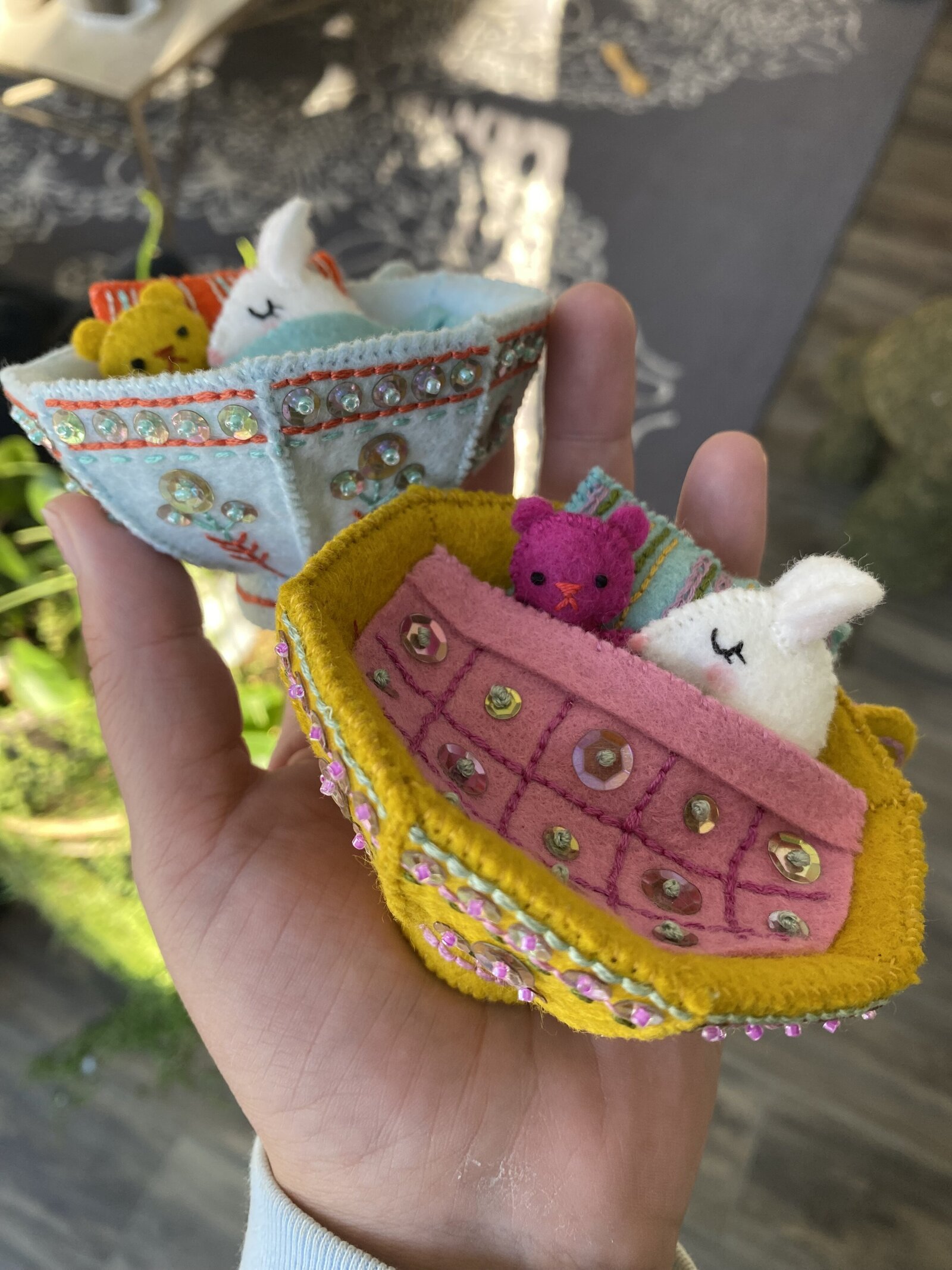 A hand holding two tea cup ornaments made out of felt with sleeping mice tucked inside.