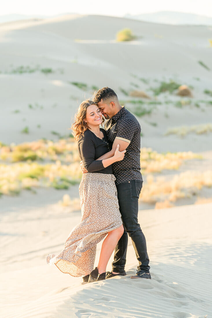 A closeup of an engaged couple with their arms around each other while standing on a sand dune at Little Sahara in Nephi. Captured by Utah Engagement Photographer Melissa Woodruff Photography