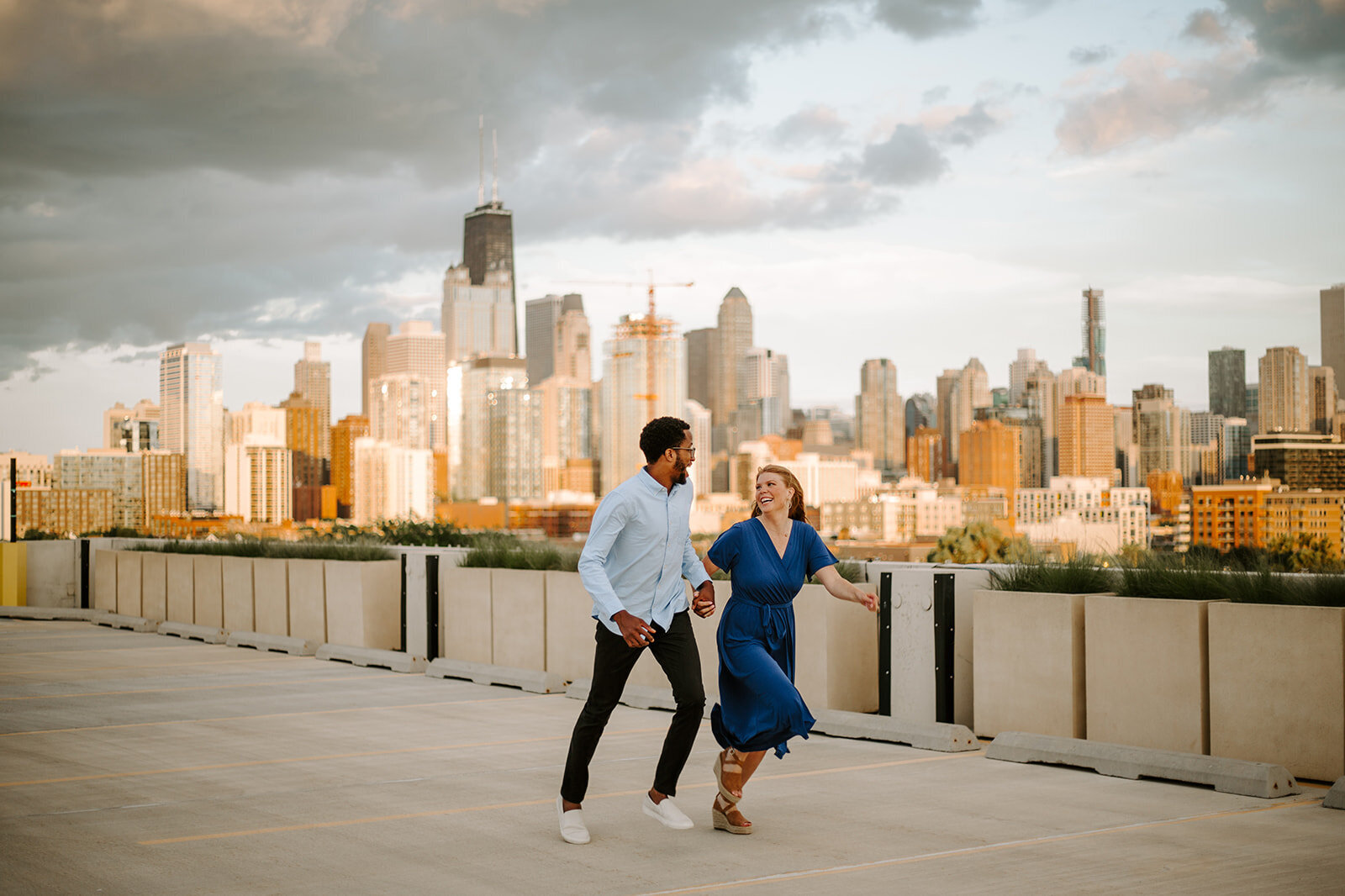 Couple holding hands running in front of the Chicago skyline during their engagement session
