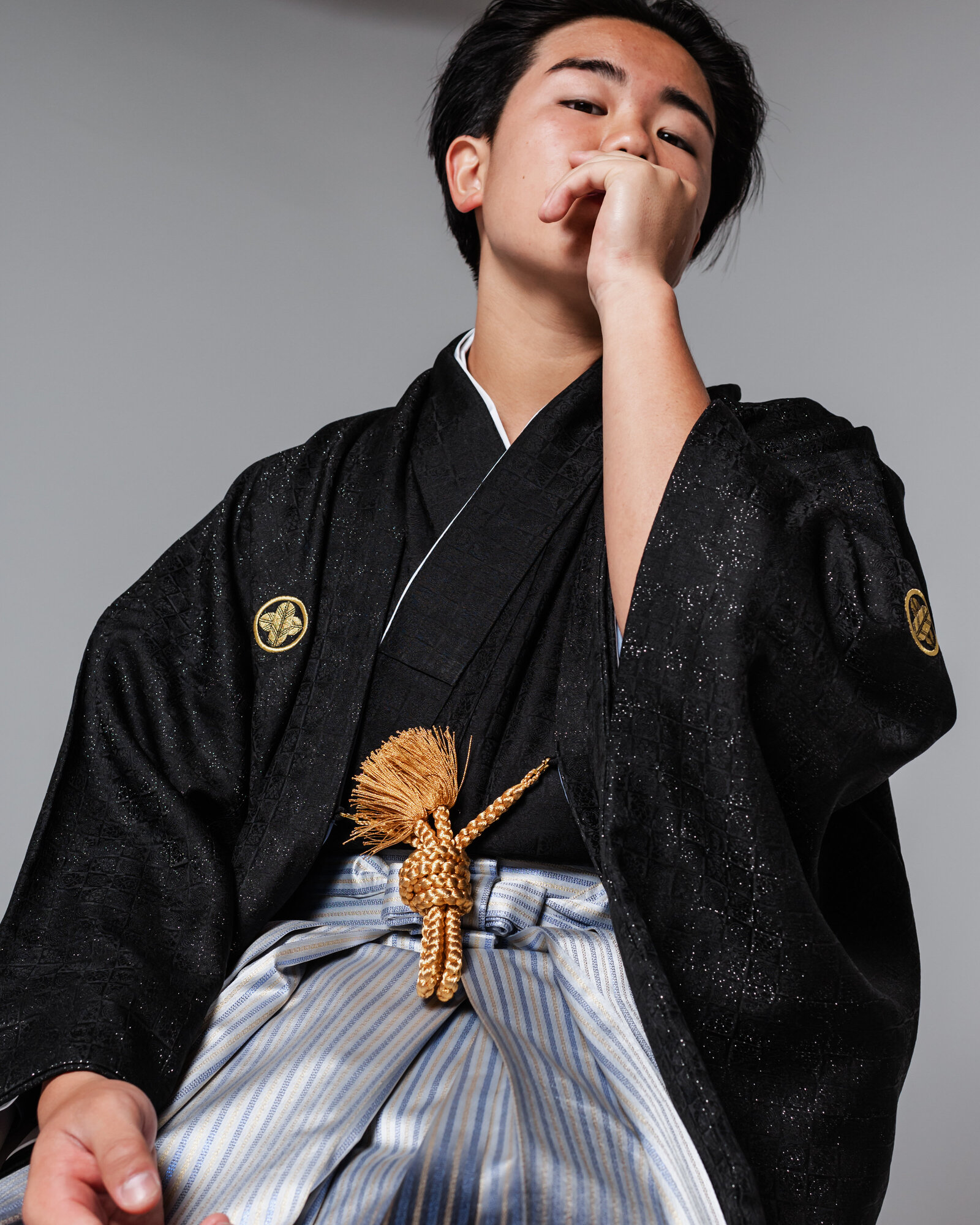 Boy in black montsuki haori with striped hakama striking a modern pose for graduation | 卒業式 黒紋付 羽織 袴 男の子 モダンポーズ