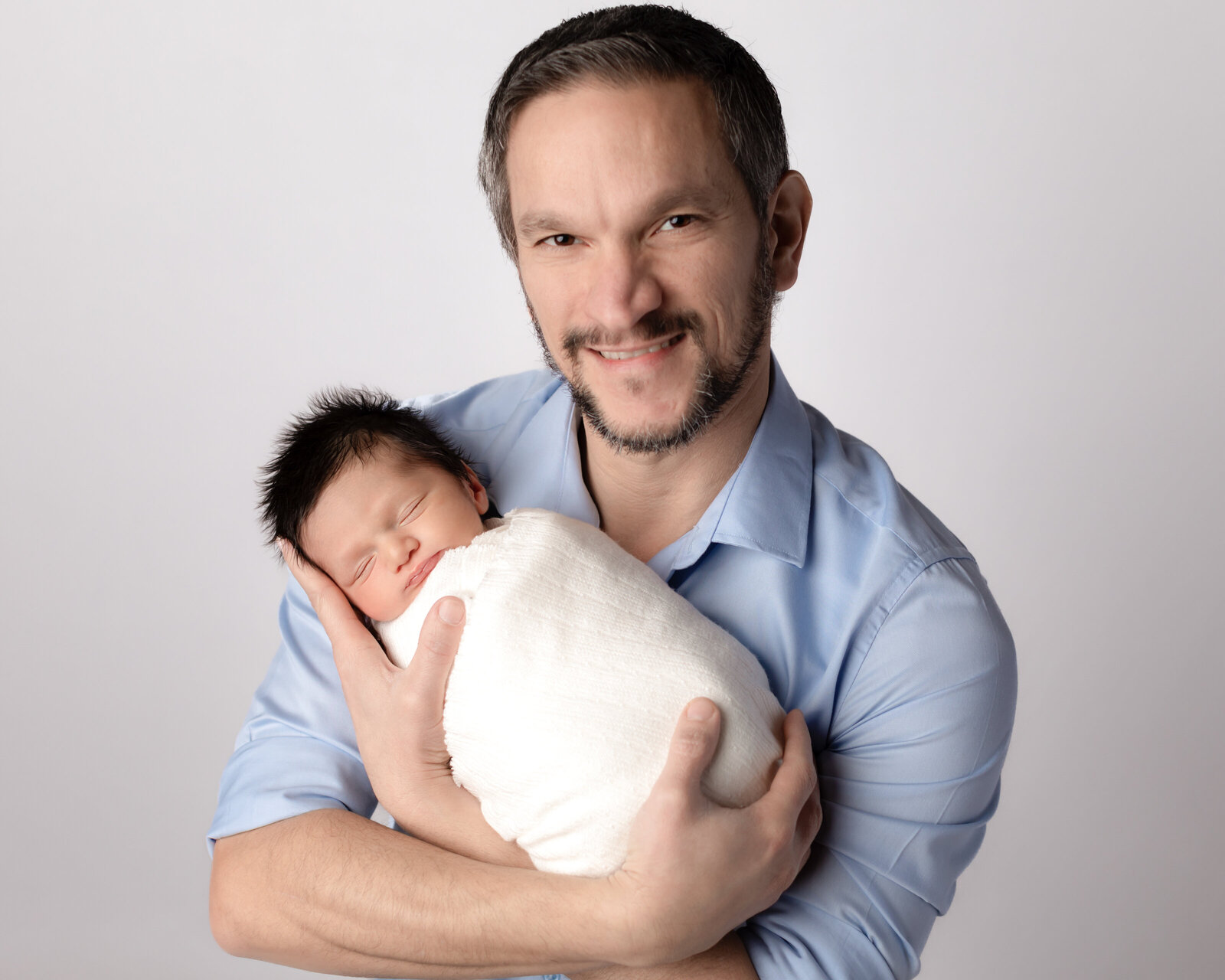 dad holding newborn son wrapped in white for studio portraits