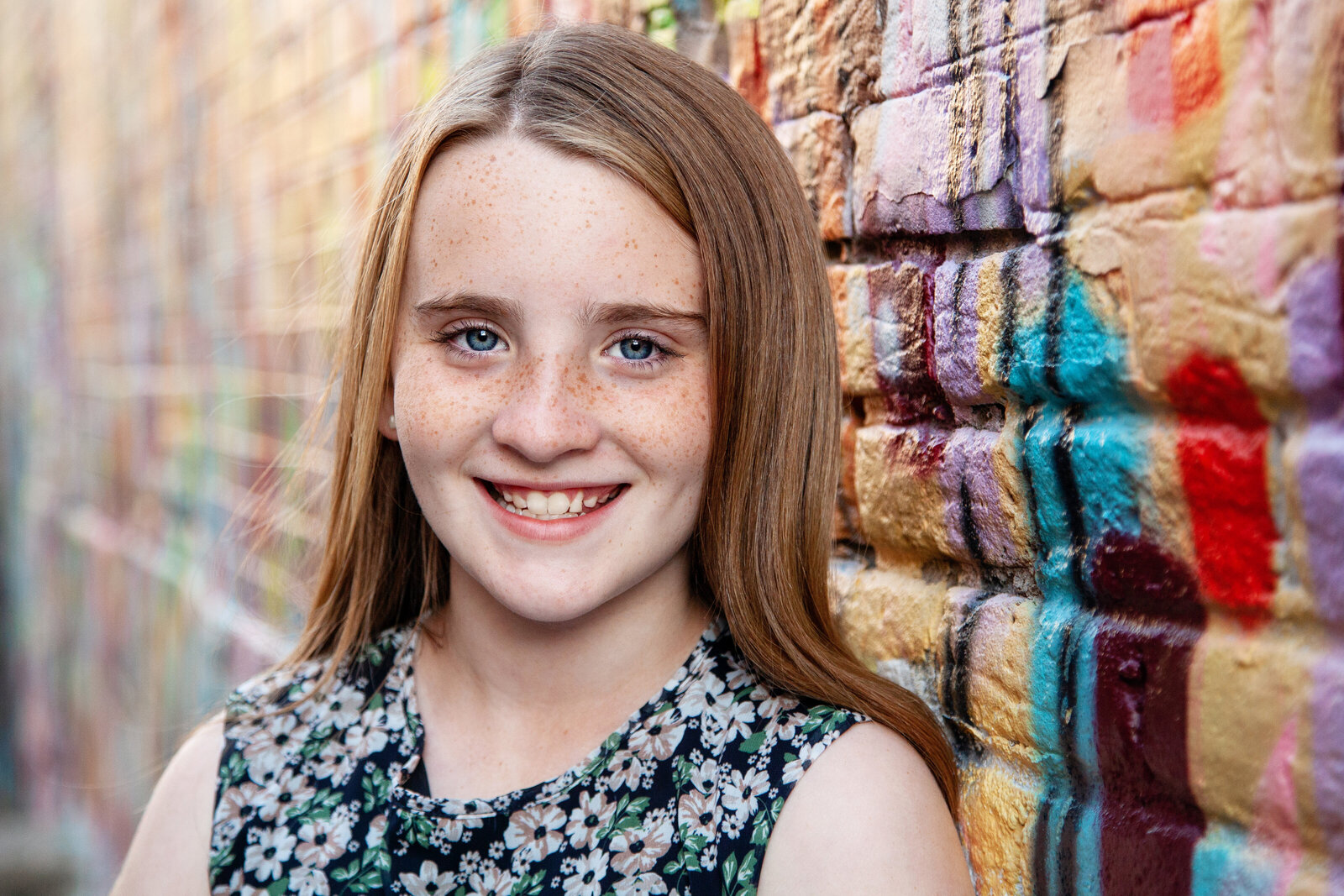 Close up of young girl in front of colorfully painted bricks.