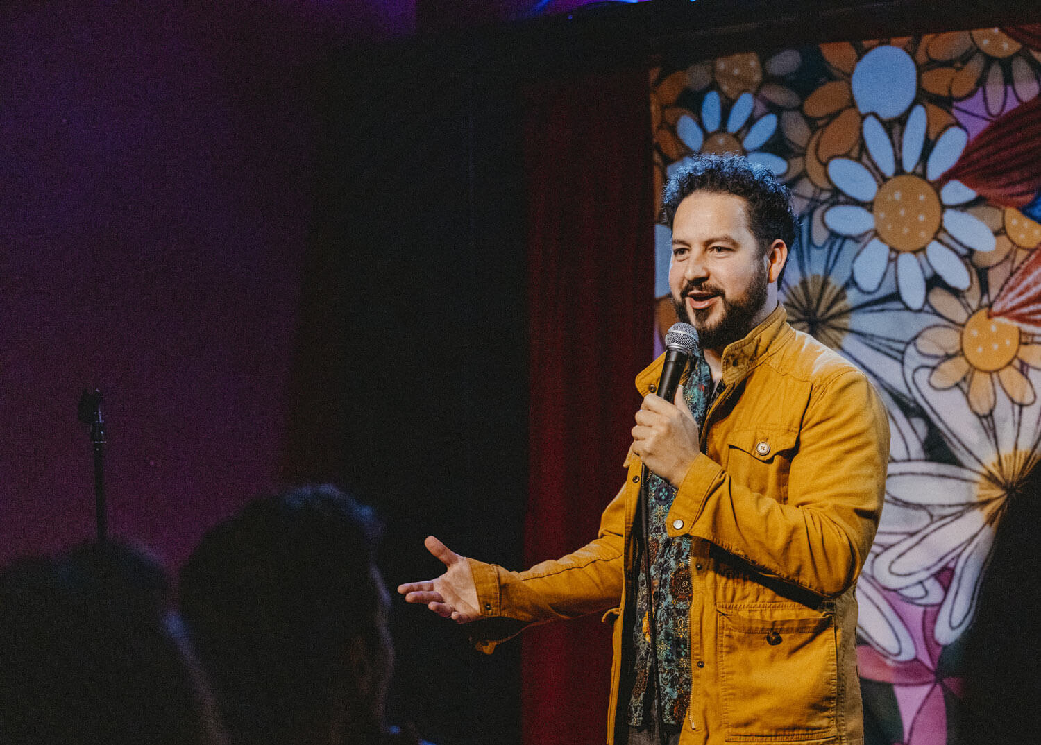 Photo of comedian, Ahmed Bharoocha, on stage and holding a microphone