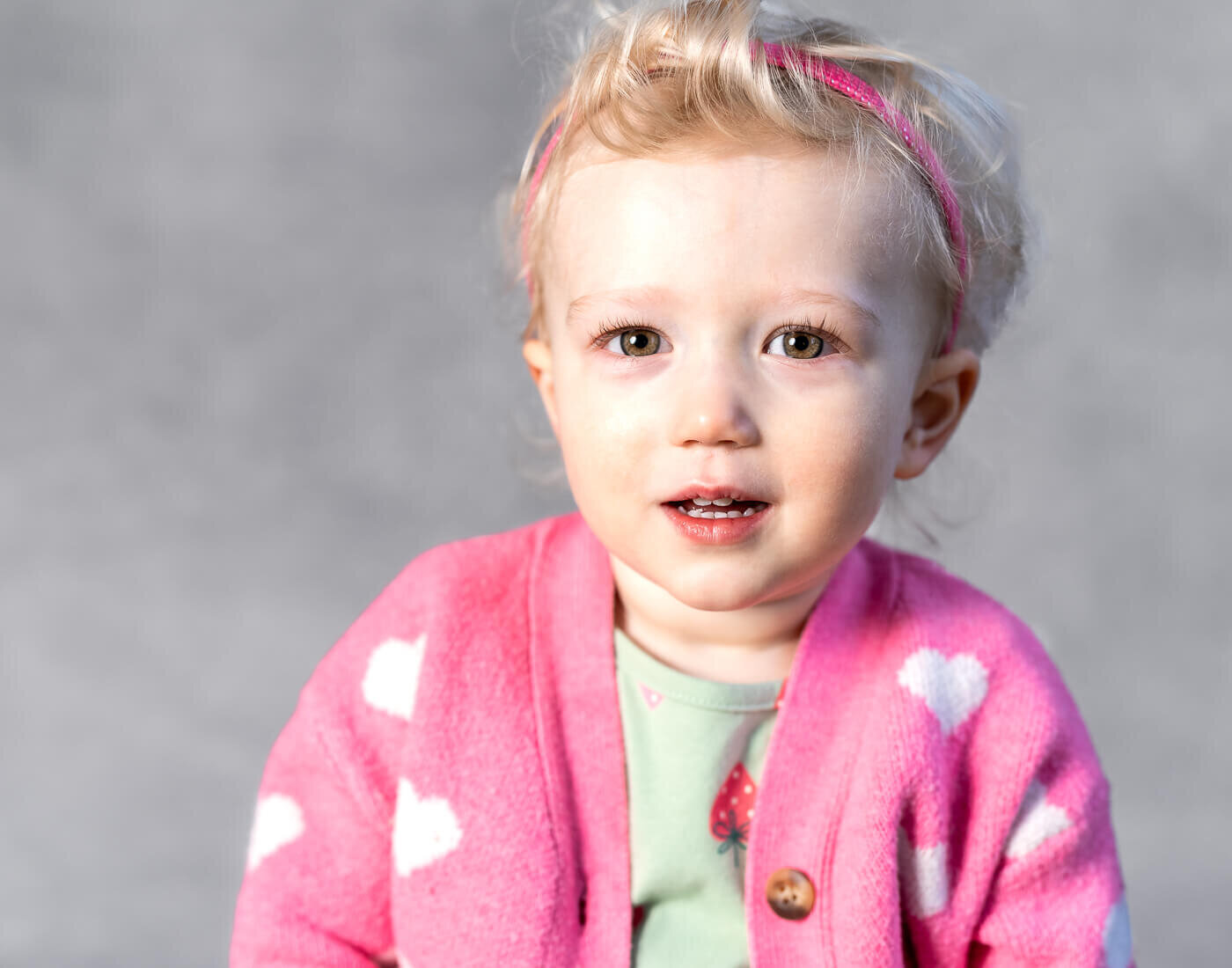 A child in a pink heart sweater smiles.
