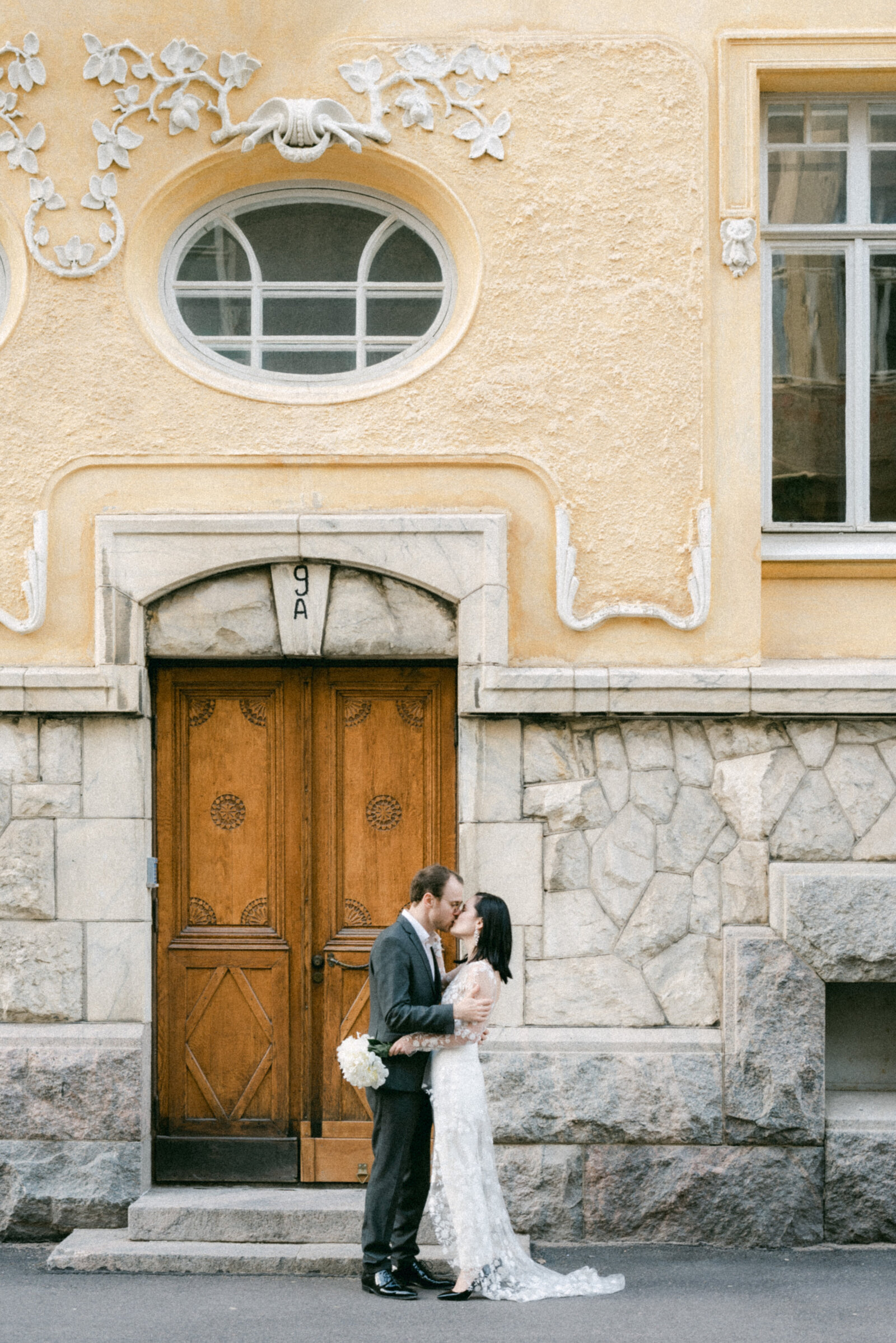 Hääpari on hääkuvauksessa Katajanokalla. He seisovat kadulla rakennuksen edessä. hääkuvaaja Hannika Gabrielssonin kuvaama romanttinen hääkuva.