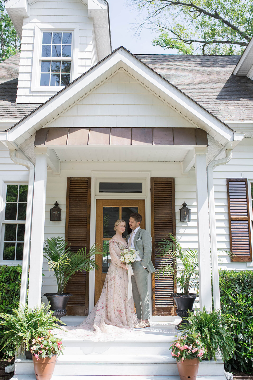 Bride and groom posing on the front porch, bride holding a white bouquet.