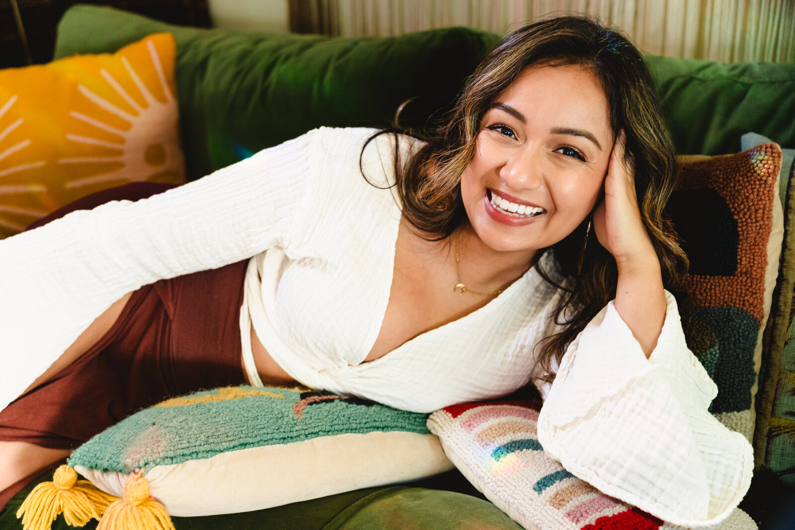 coach for women lies down in a green sofa, one of hands in her hair and smiles
