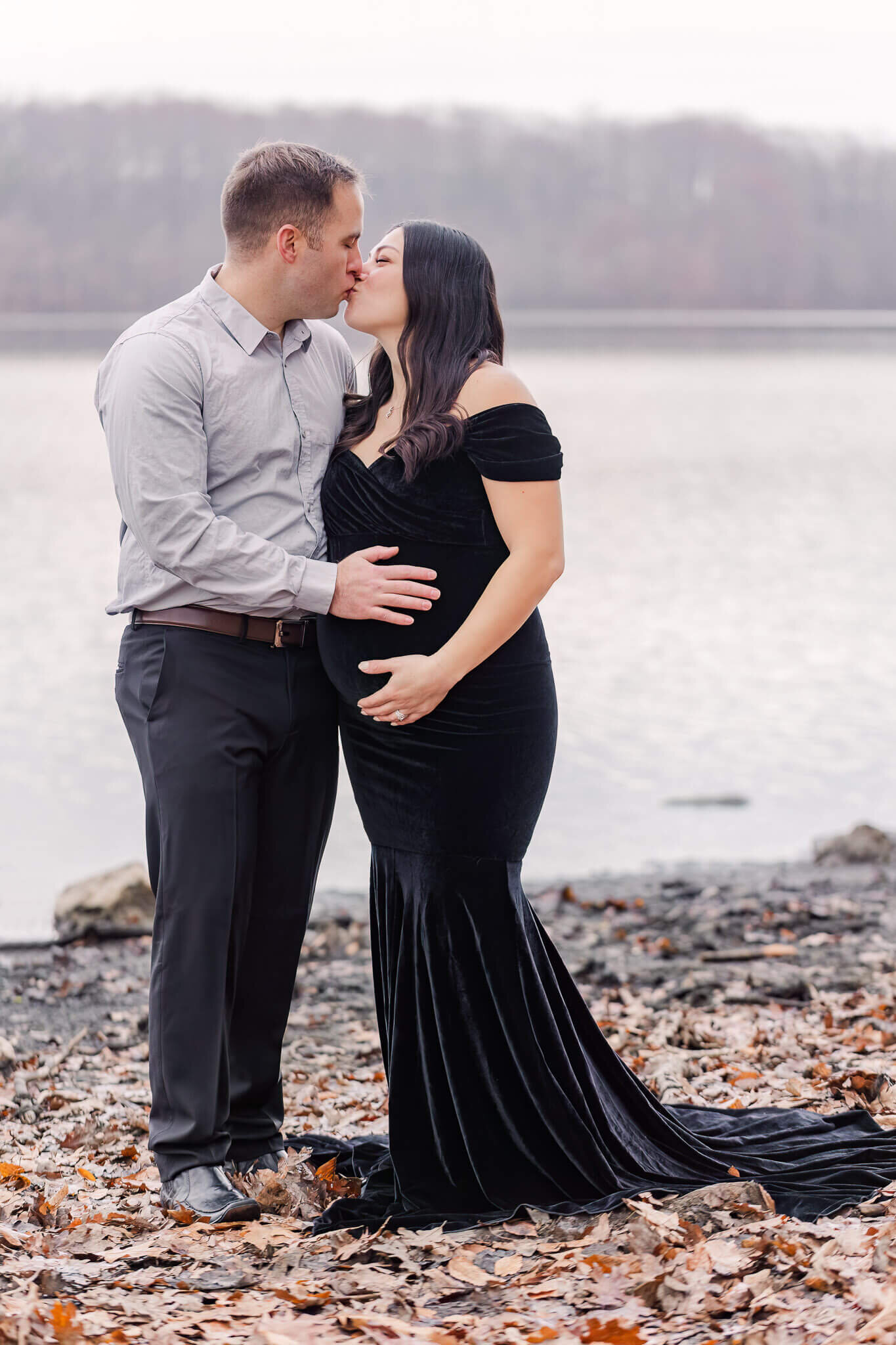 A couple posing in front of a lake during their maternity photography session.