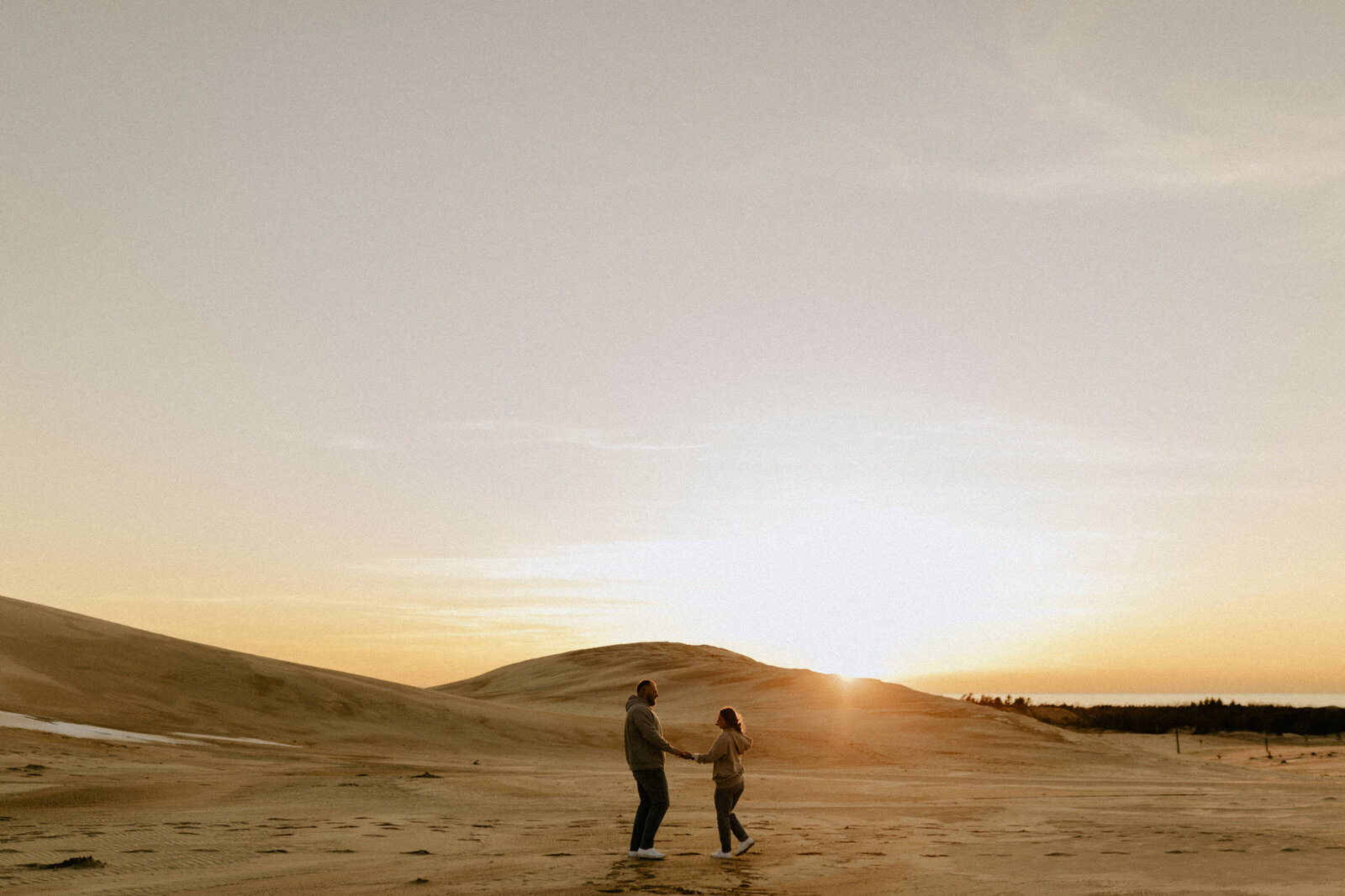 Wide shot of a couple holding hands at Silver Lake Sand Dunes during sunset