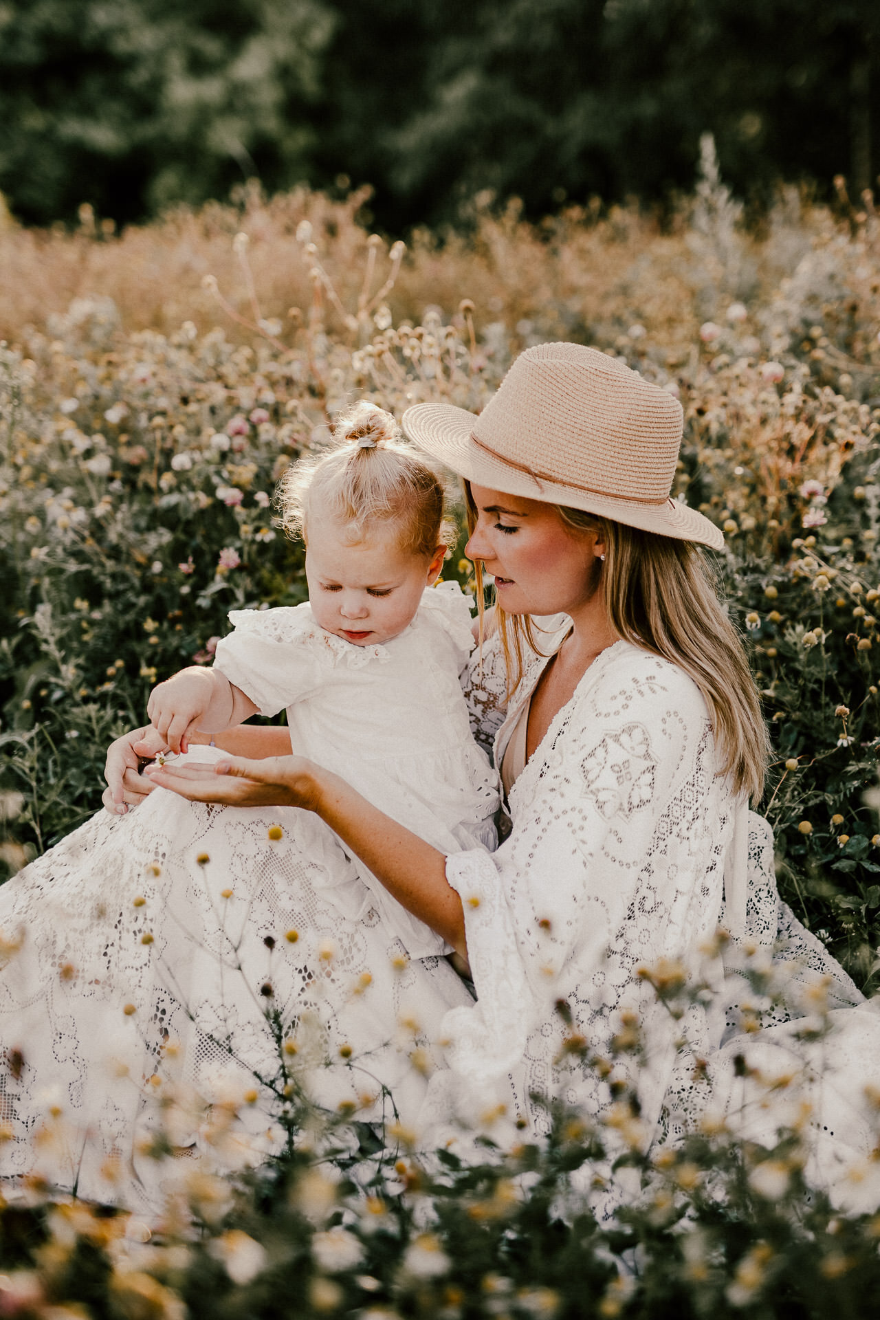 en mamma och dotter sitter på ett blomfält och plockar blommor