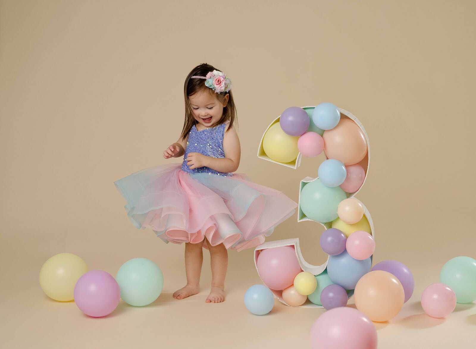 Birthday girl twirling dress around pastel balloons on floor and balloon filled #3 marquee. Photographer at Atlanta Birthday photo studio.