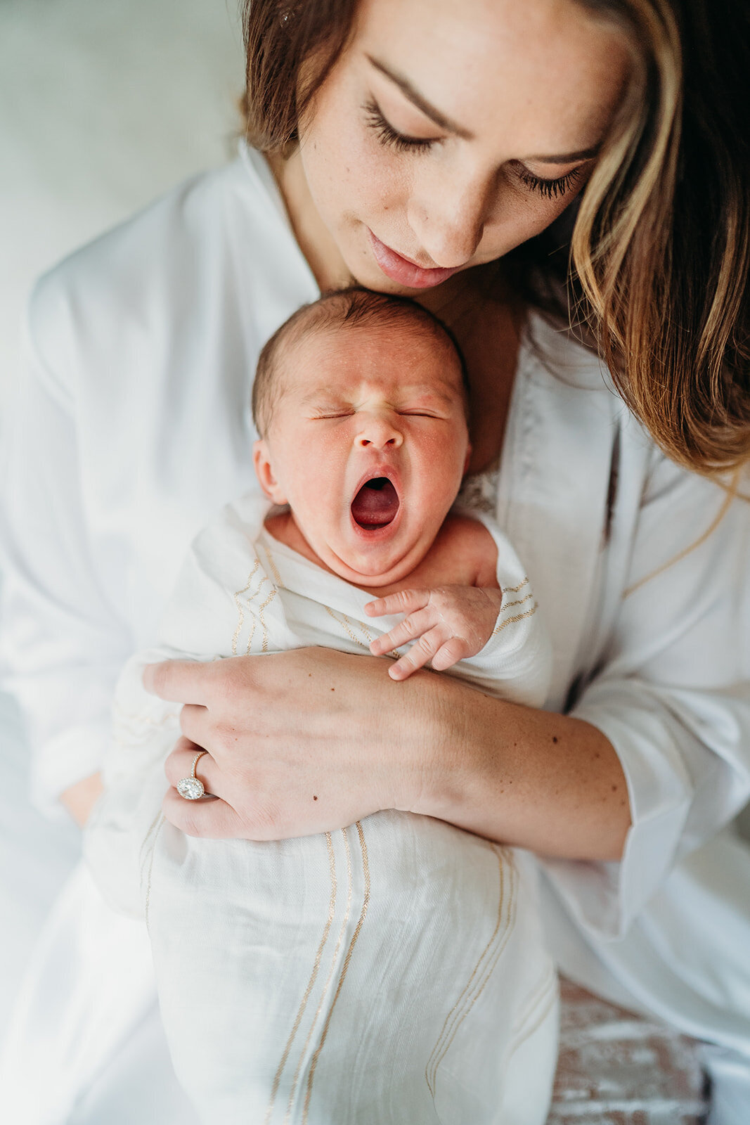 mother in white bathrobe holds yawning newborn