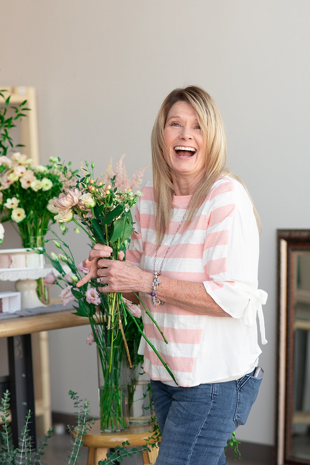 Florist wearing jeans and a striped white a coral shirt laughing while selecting flowers