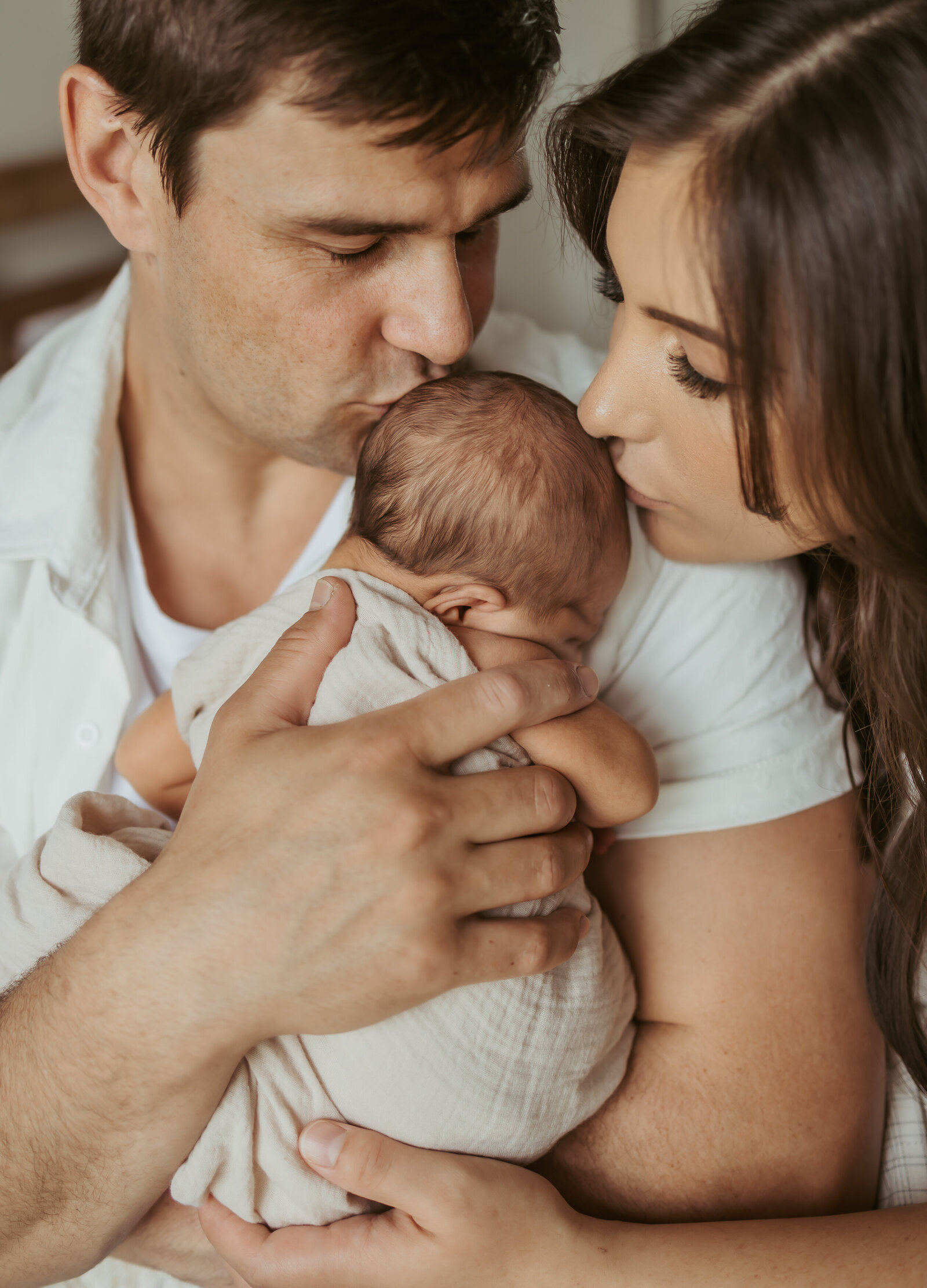 A relaxed In-home photography session with a new family where parents are kissing the head of their newborn baby.