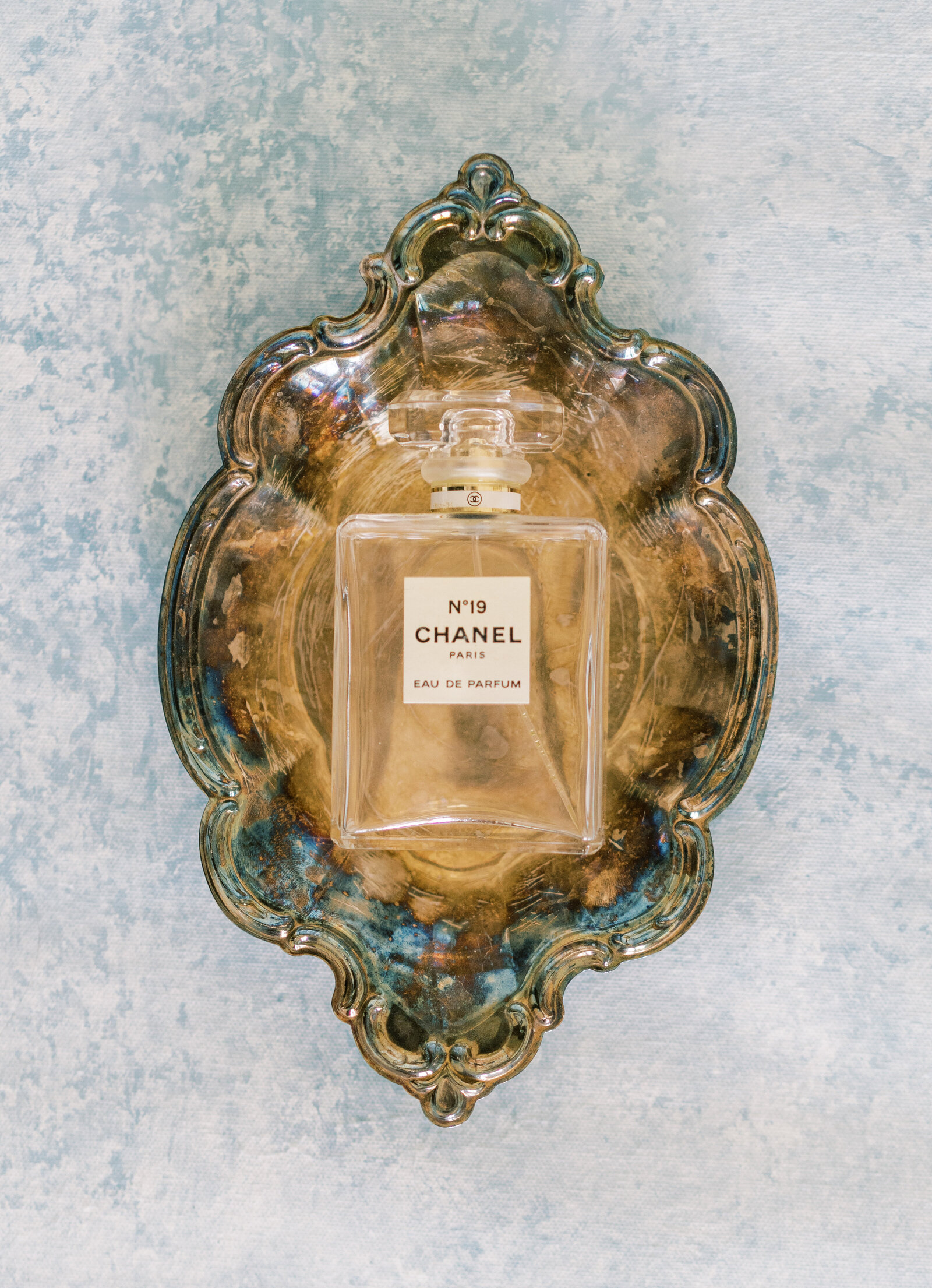 Portrait of a Chanel No.19 perfume bottle atop a bronze antique dish