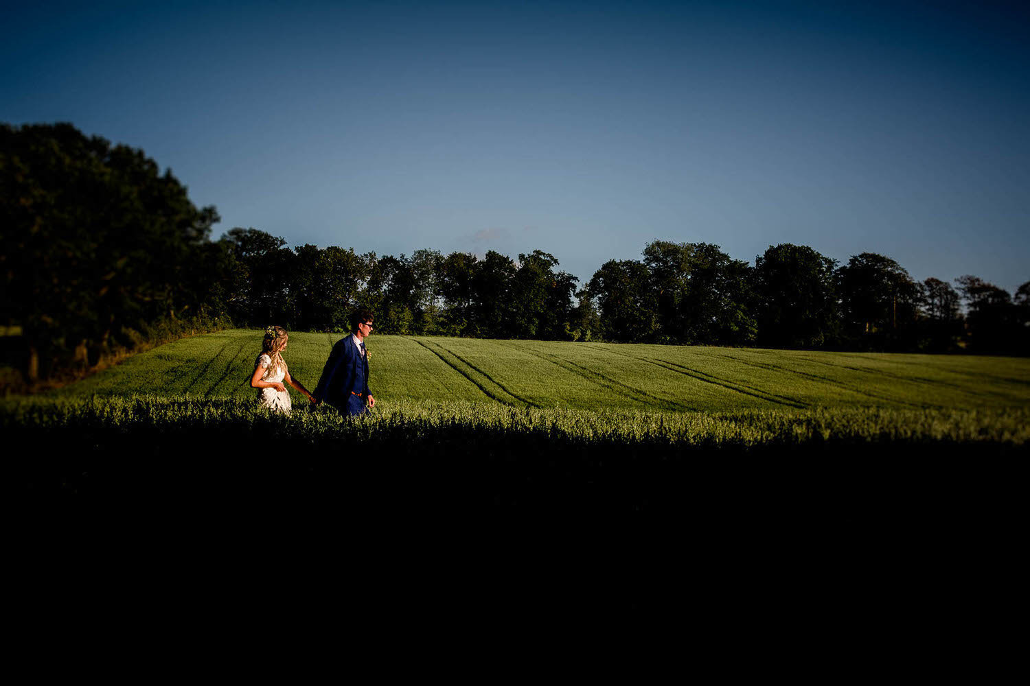 bride and groom walking throuigh the corn fields in cumbria at blaithwaite house