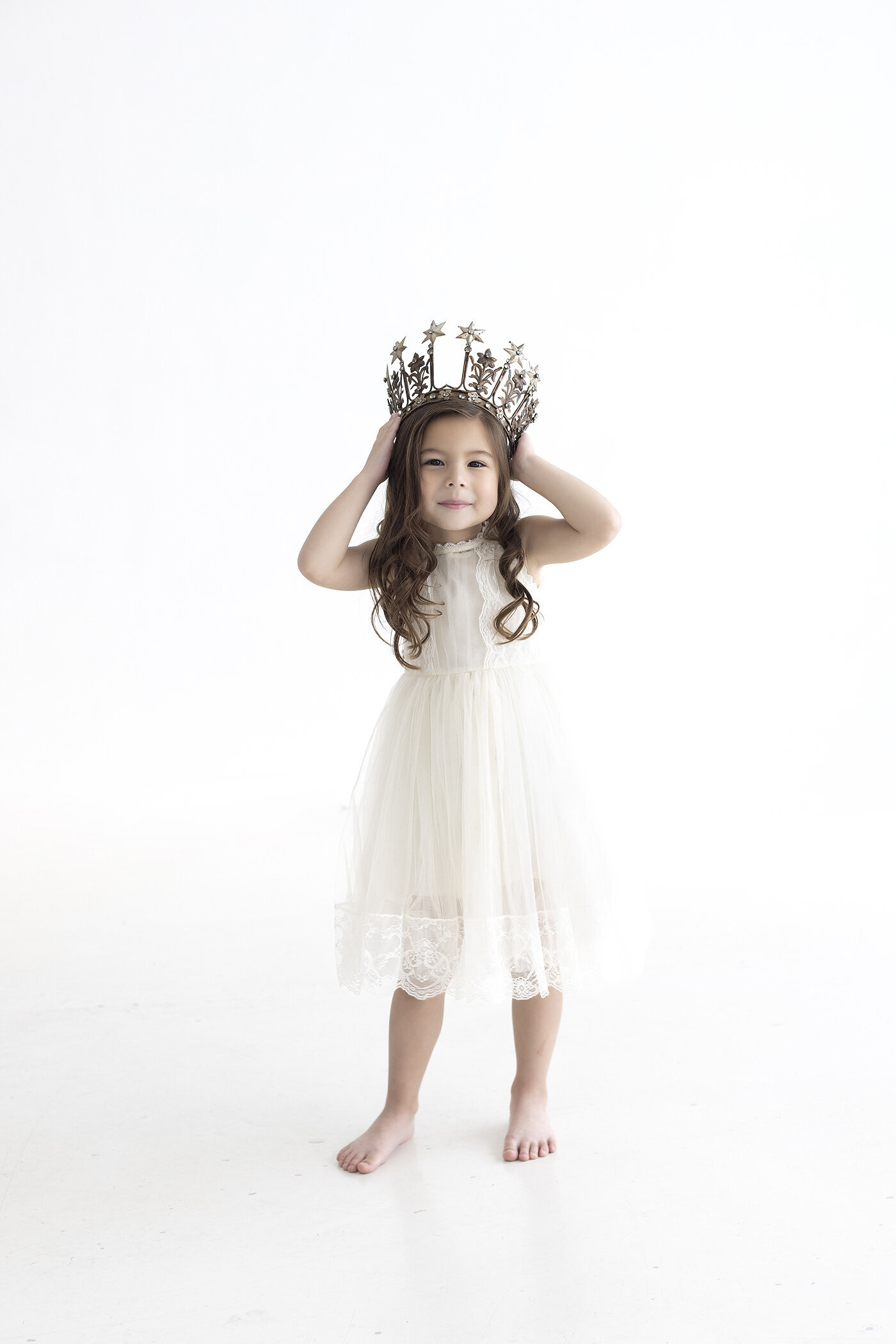 Photo of a young girl holding a crown on her head.