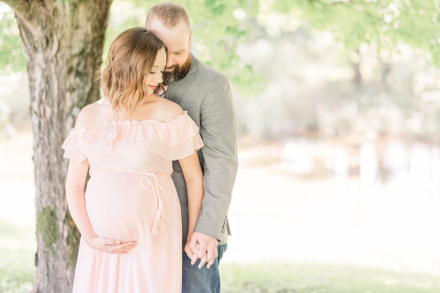 A man standing behind a woman, holding her hand as she holds her baby bump with the other hand.