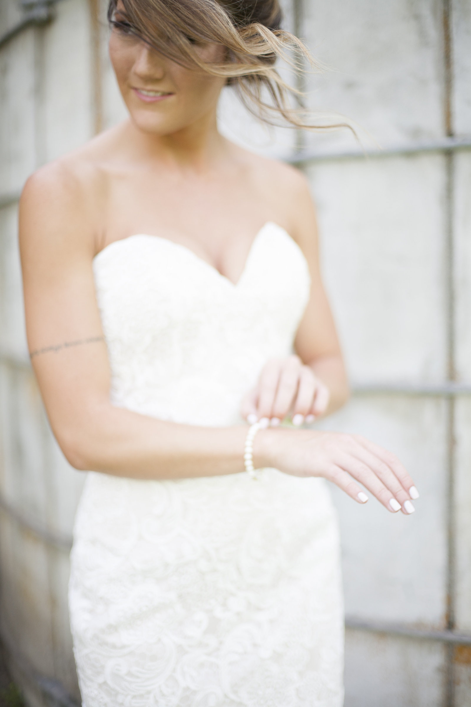 A bride in a sleeveless wedding dress, holding a bracelet.