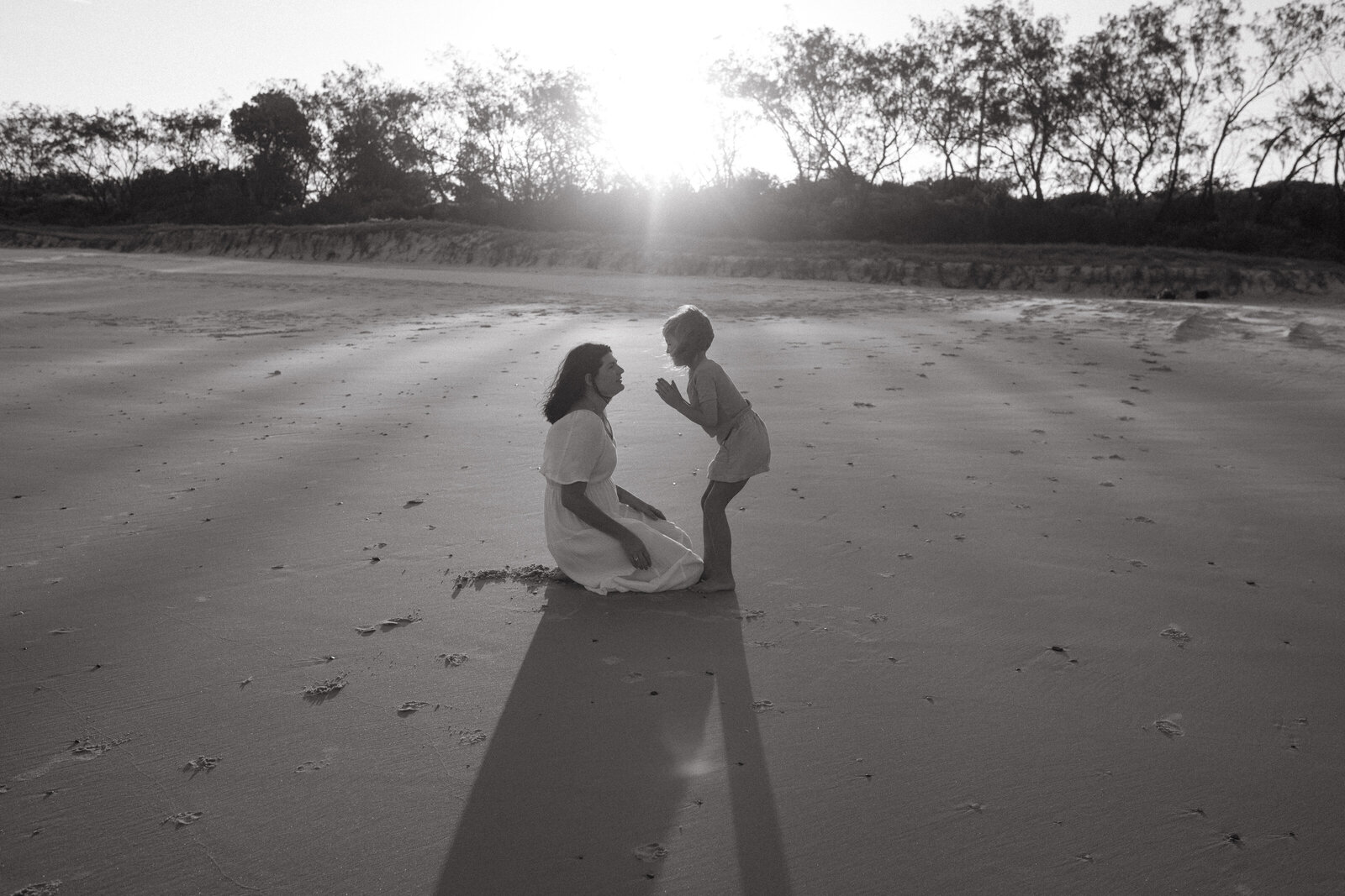 A mother and daughter share a story in the sunset light , the dunes of Pottsville beach are covered in sunset light with cassaurina trees are softly filtering the light