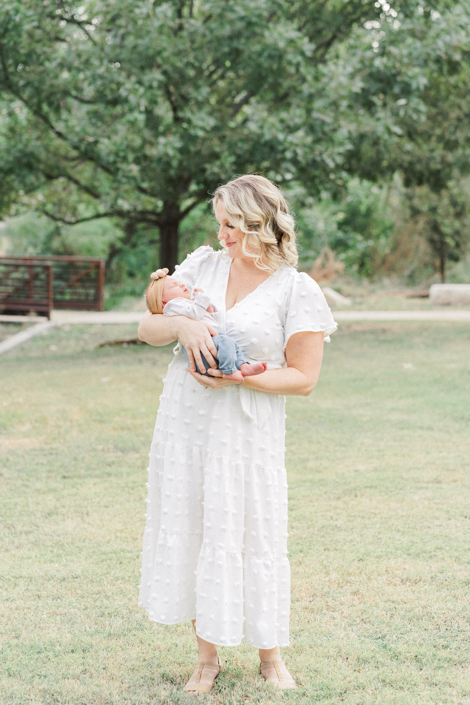 a mother stands in a field at Katherine Fleischer park. She holds her baby in a cradle position. 
