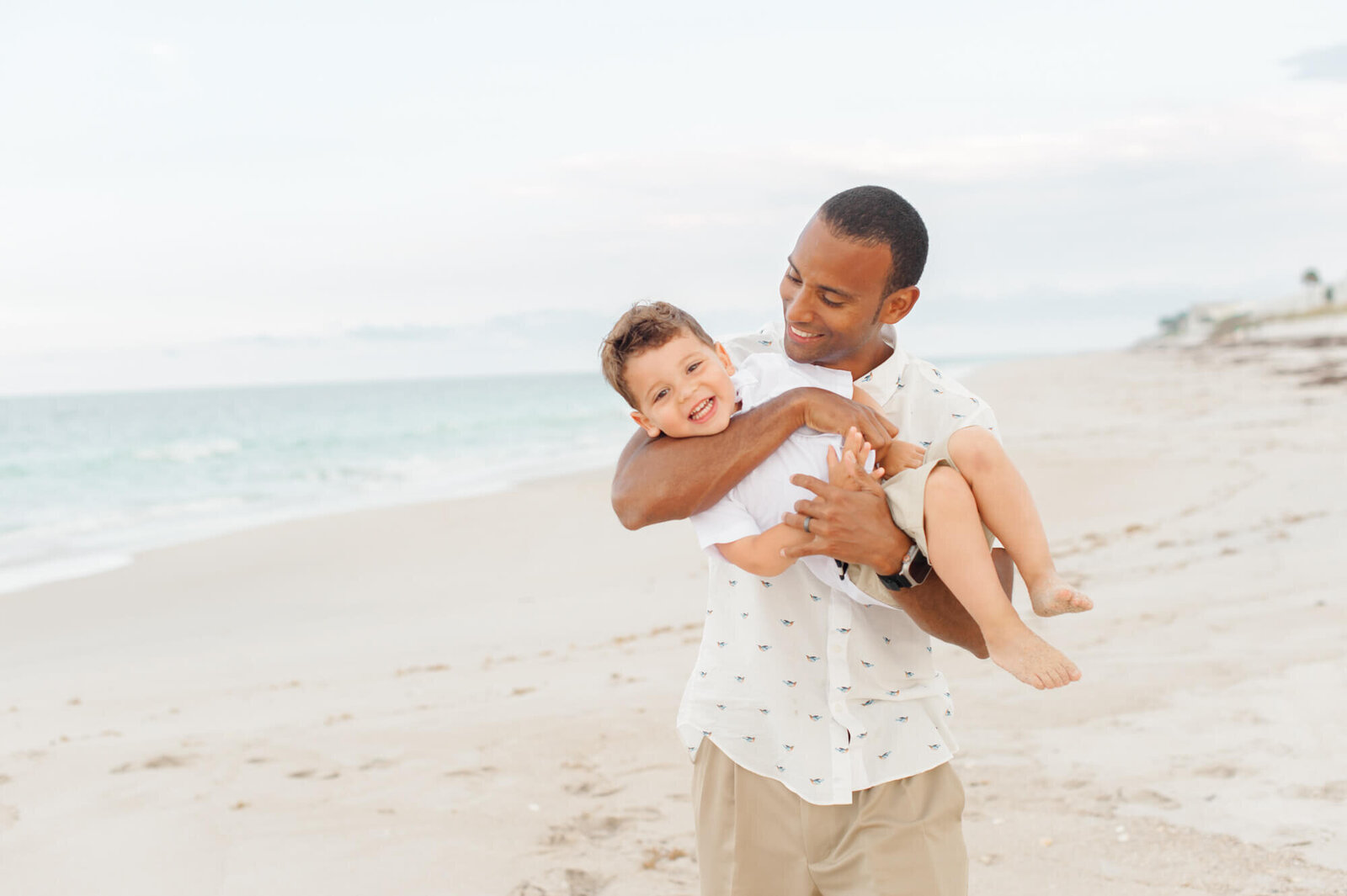 Dad tickles young son while holding him on the beach during their family photo session