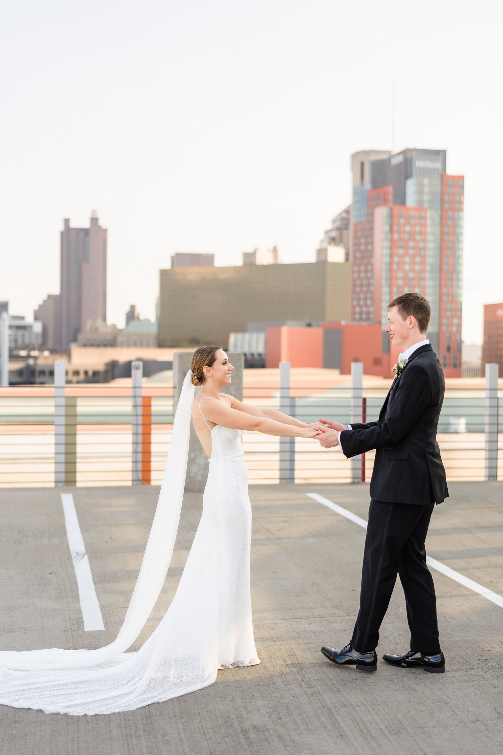 Bride and groom hold hands and smile at each other on the rooftop of a parking garage overlooking downtown Columbus