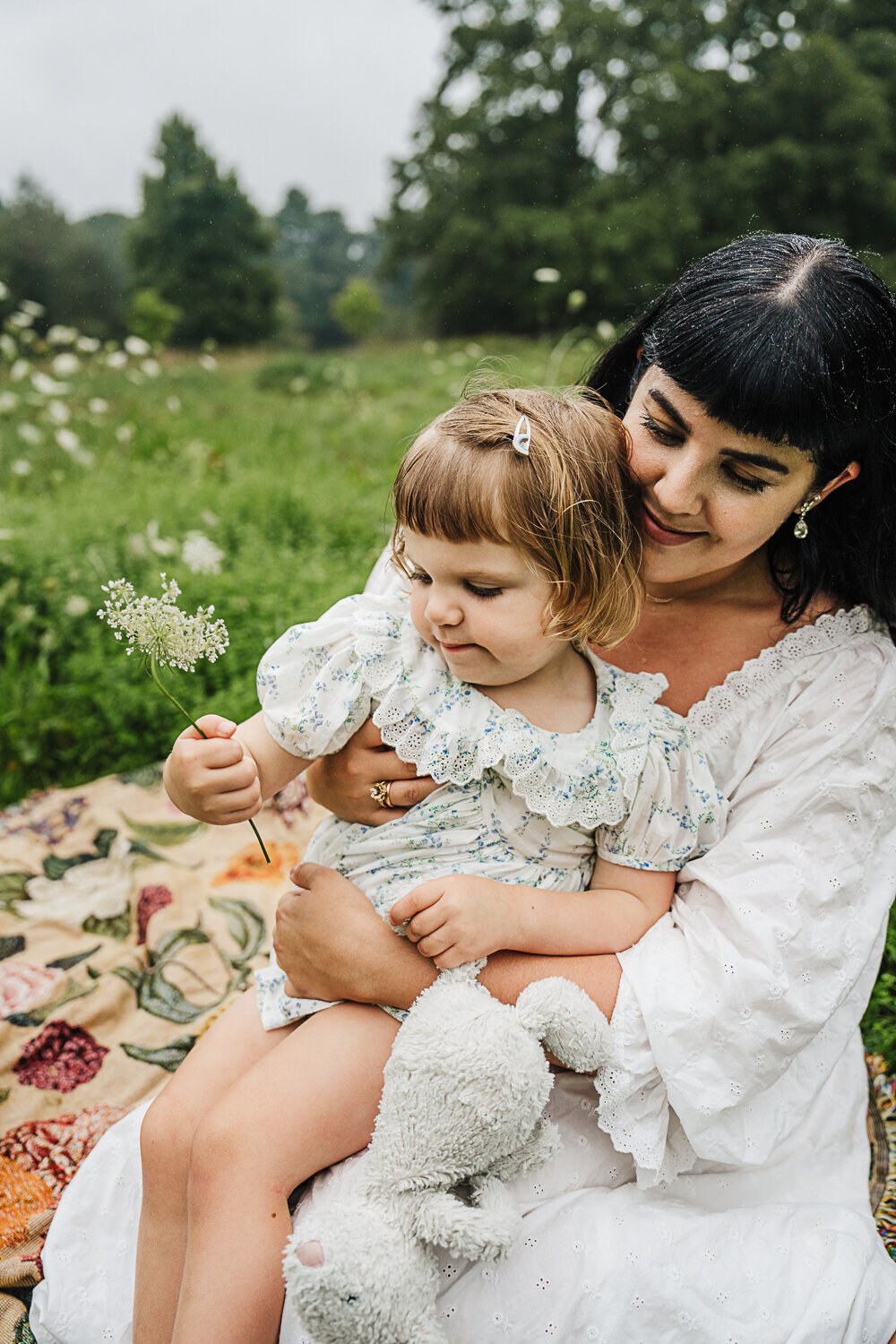 toddler girl sits on moms lap and holds queen annes lace