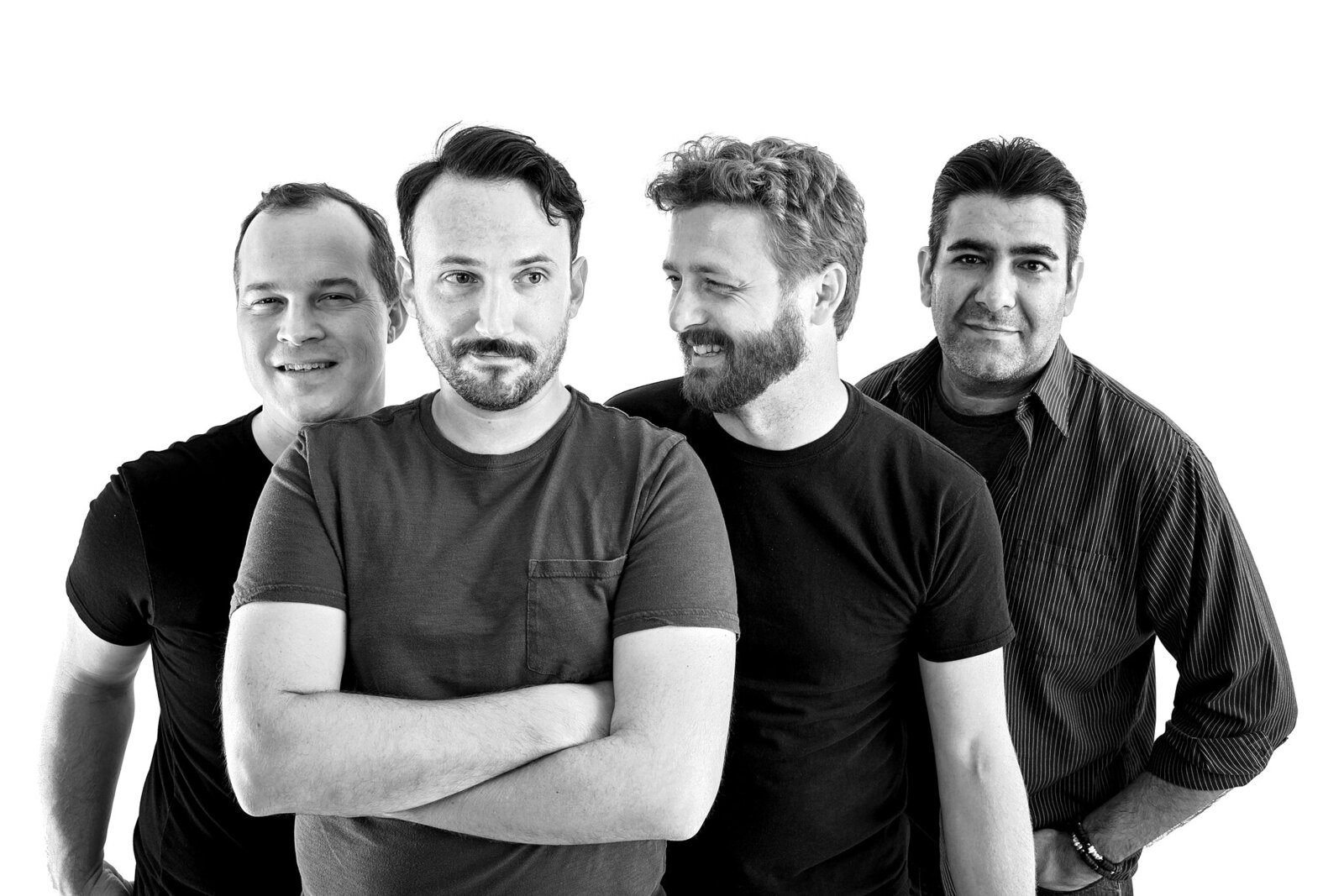 Four men stand closely together against a white background in this professional band photo. Three smile while the man in front, arms crossed, looks serious. All wear casual shirts in this black and white image—perfect for music photography Jacksonville.