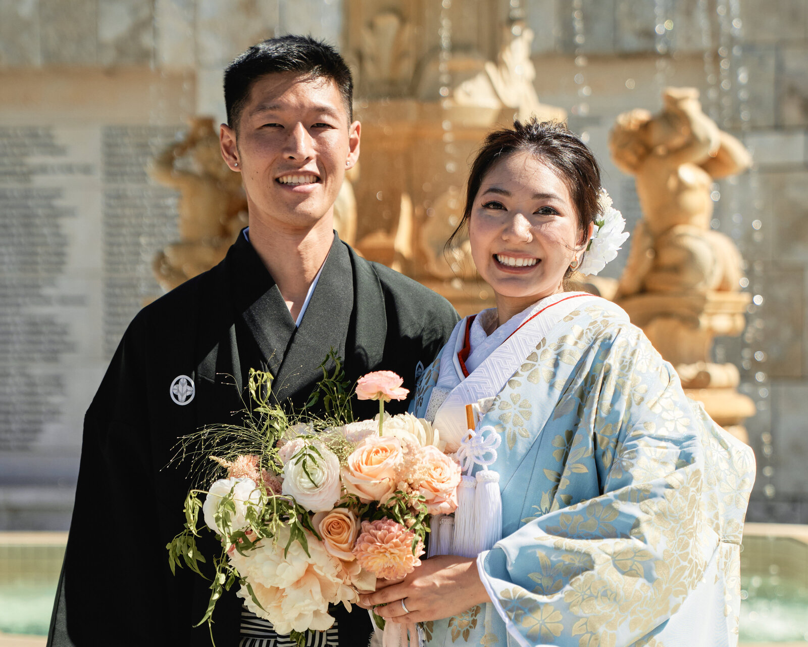 Orange County kimono rental wedding – bride in pale blue gold-pattern uchikake kimono and groom in black montsuki by a stone fountain, kimono rental |
オレンジカウンティーの噴水前、青と金の打掛着物レンタル花嫁と黒紋付袴の新郎
