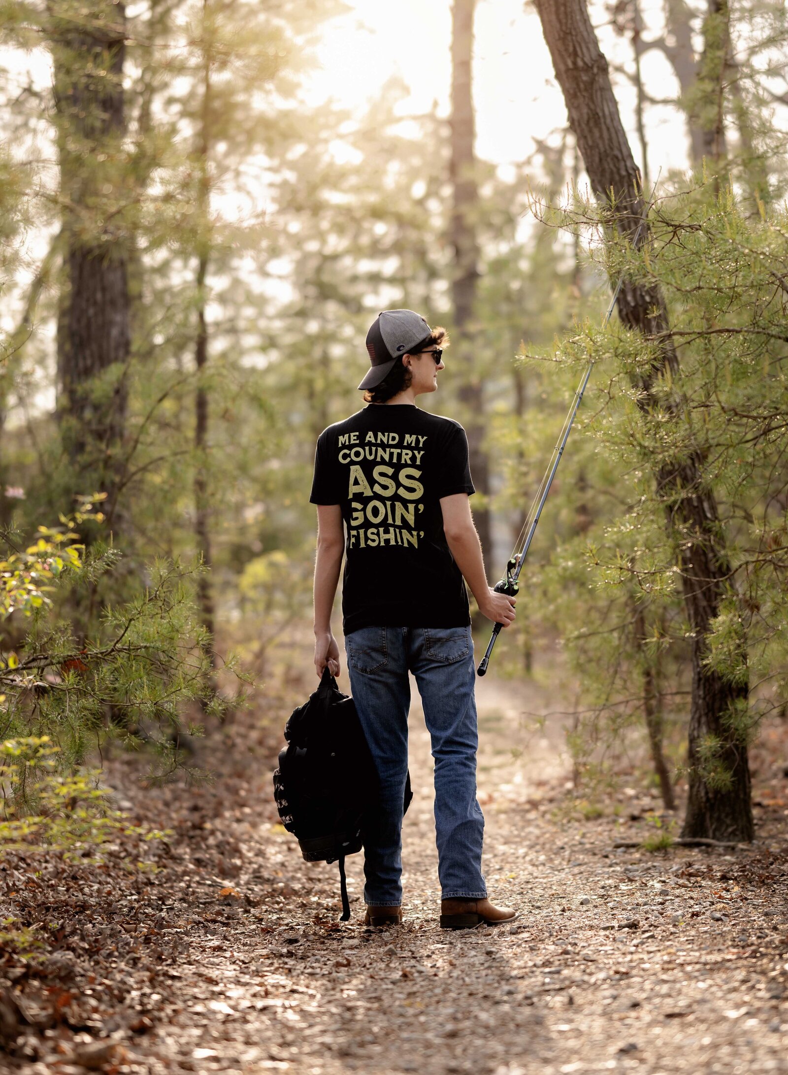 Senior photo of boy walking in woods with fishing gear. Senior graduation photos taken by Jenni Nikki Photography in Atlanta, GA