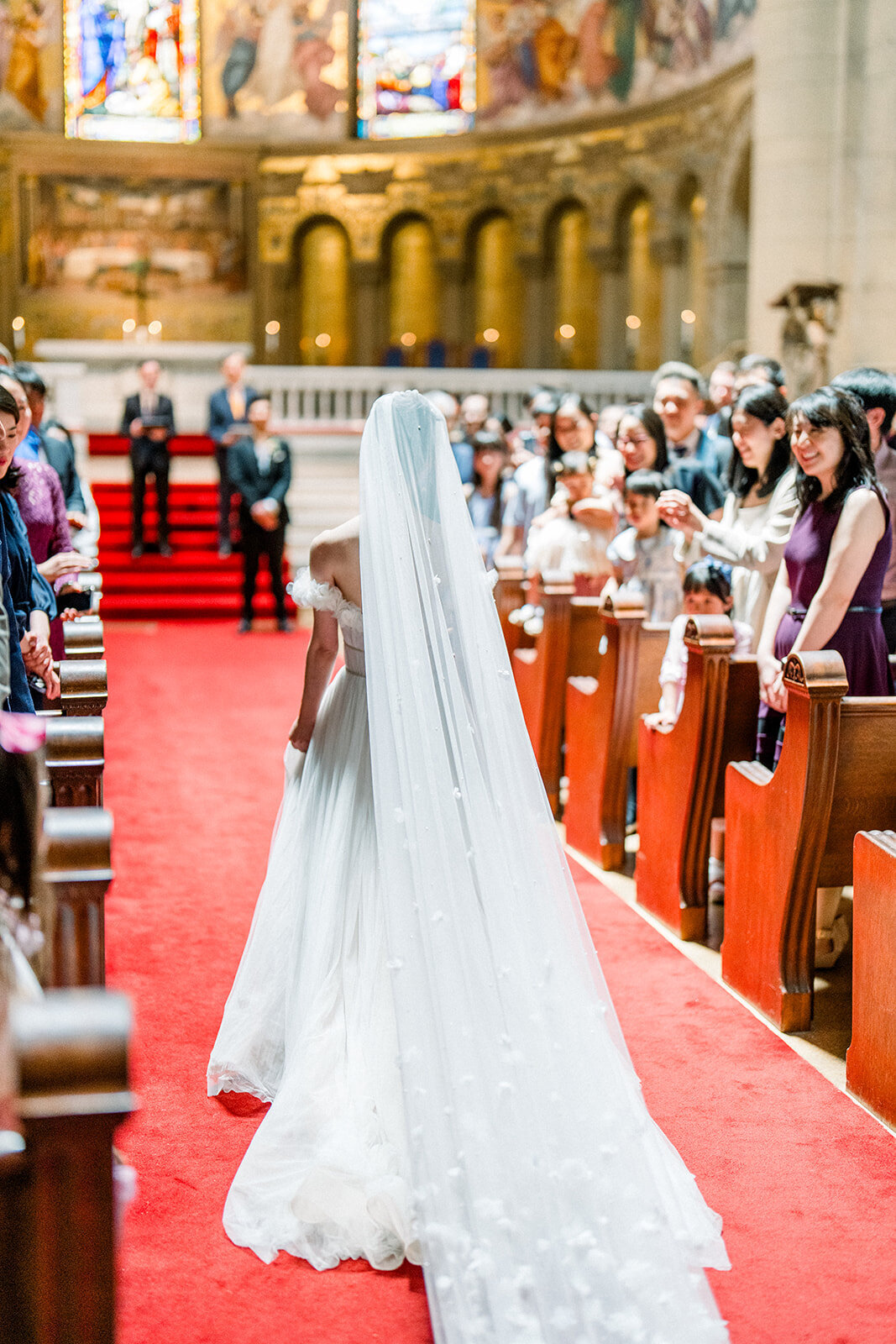 The bride makes a grand entrance as she walks down the aisle of Stanford Memorial Church, surrounded by loved ones.