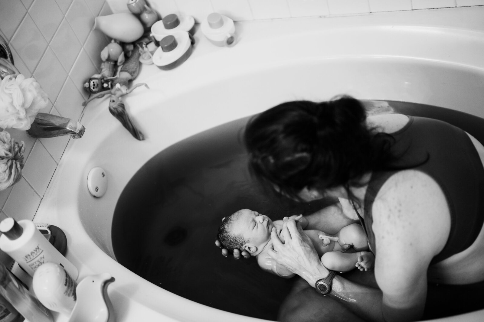 Mother holding her newborn in a birth pool moments after delivery — peaceful home-birth photography in Fort Worth by Poppy + Blue Photography