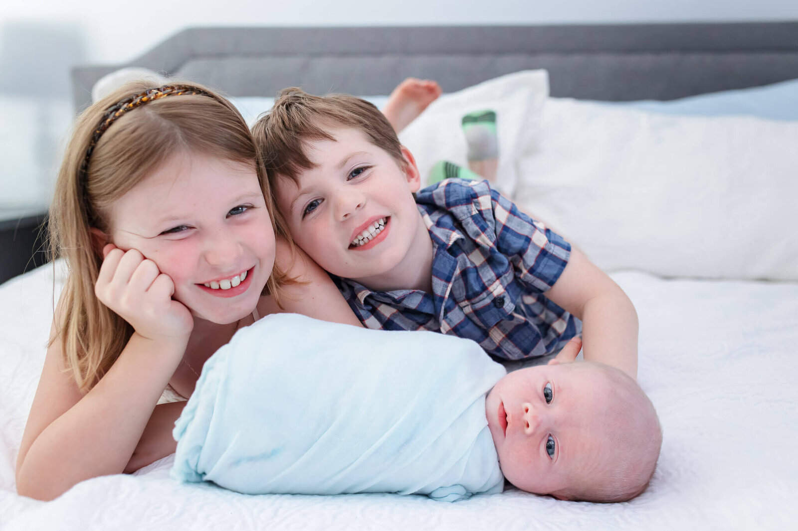 A brother and sister laying in bed with their newborn baby brother.