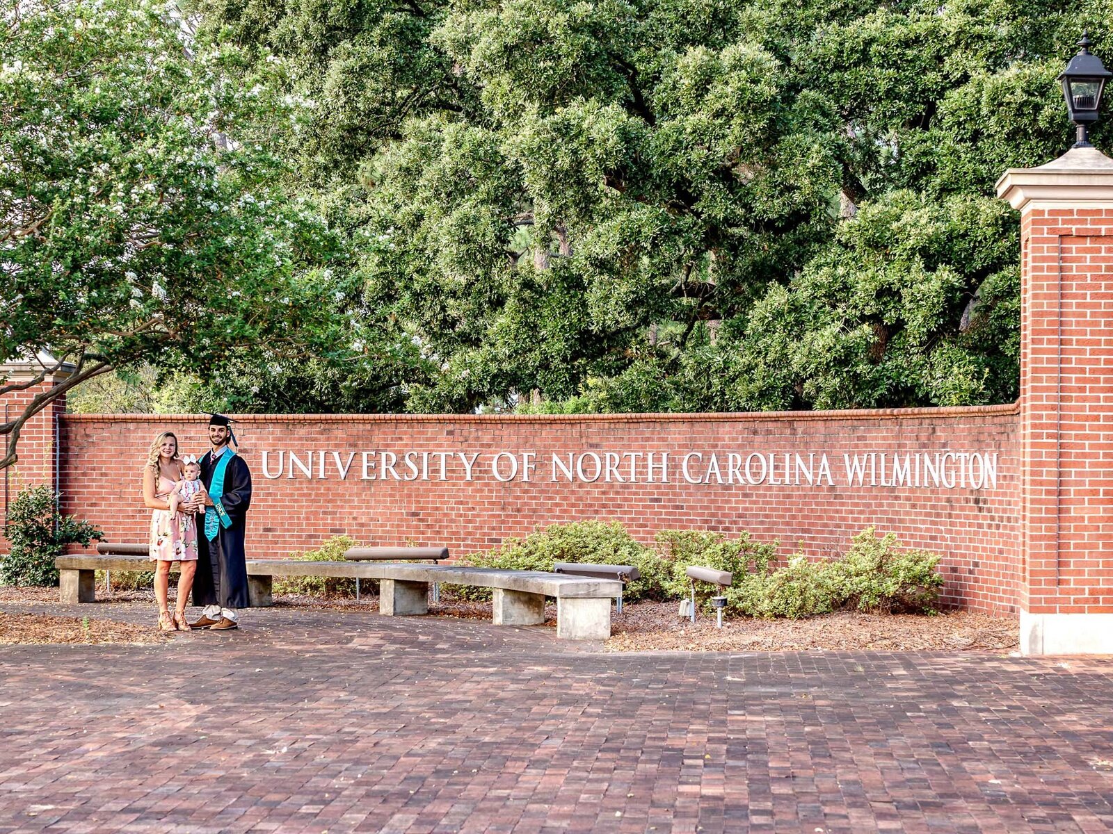 A graduate with family standing in front of the University of North Carolina Wilmington sign. This image captures the joy of academic achievement, ideal for commemorating graduation with family photography.
