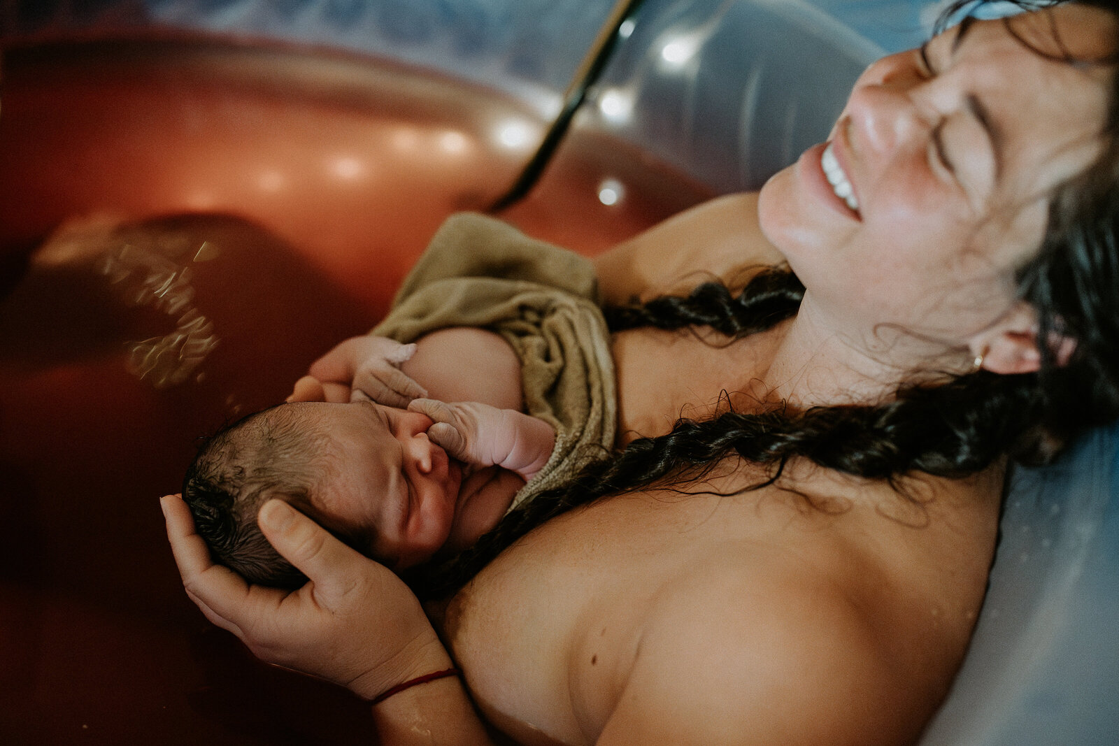 A mother expressing her profound joy after delivering her baby in a birth pool at home in City Beach. 