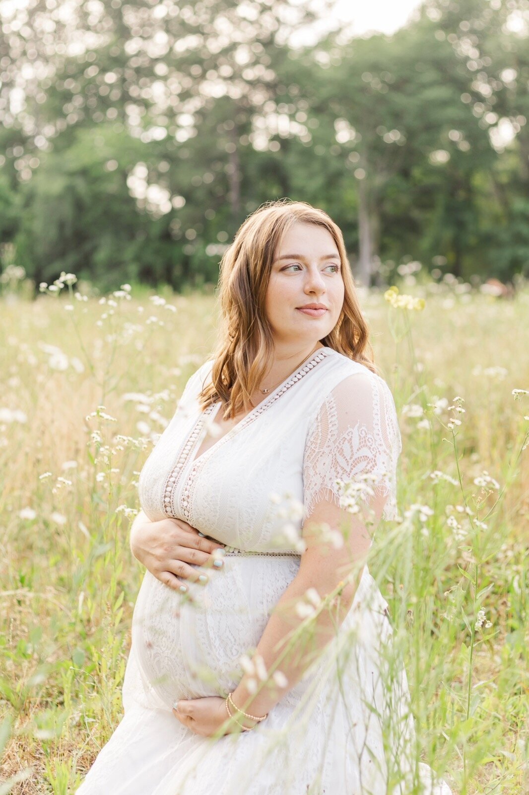 Pregnant woman kneeling in a grassy field looking over her shoulder