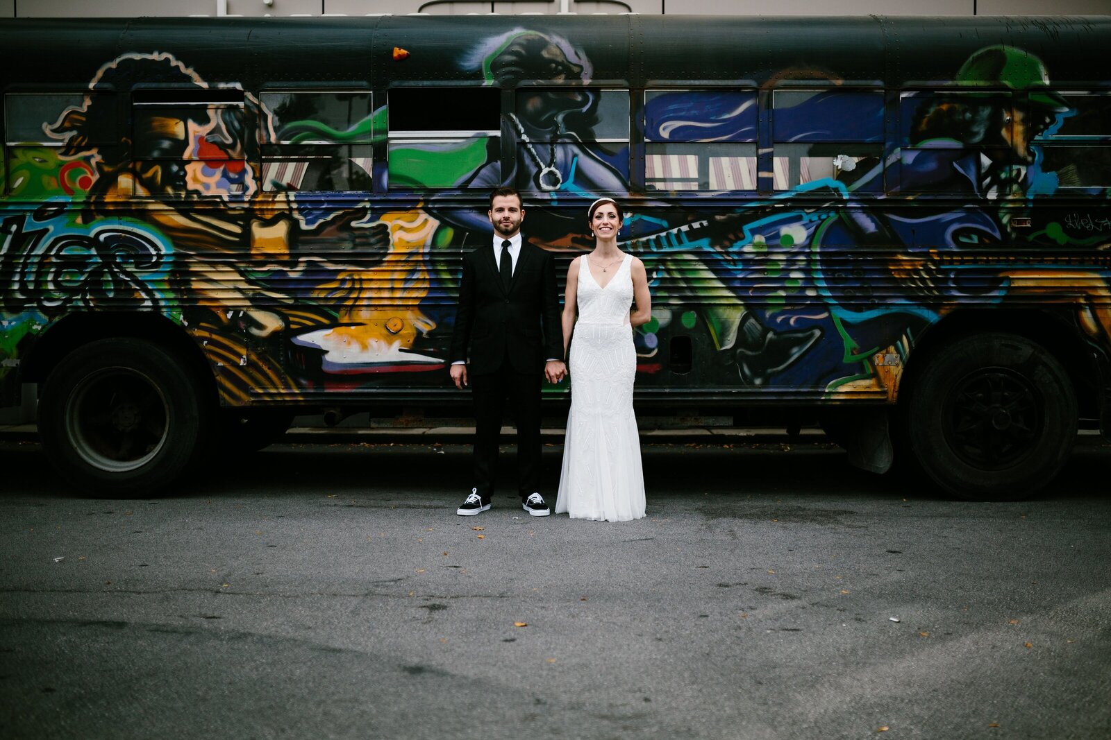Bride and groom pose for portrait in front of bus covered in graffiti