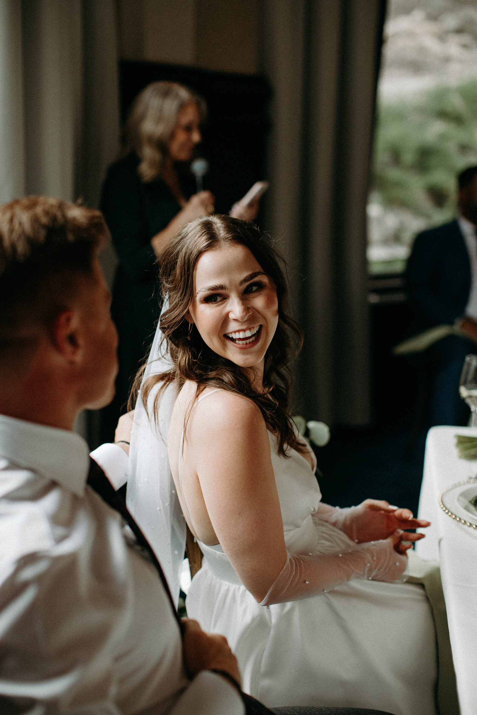 bride looking at groom with someone speaking in the background