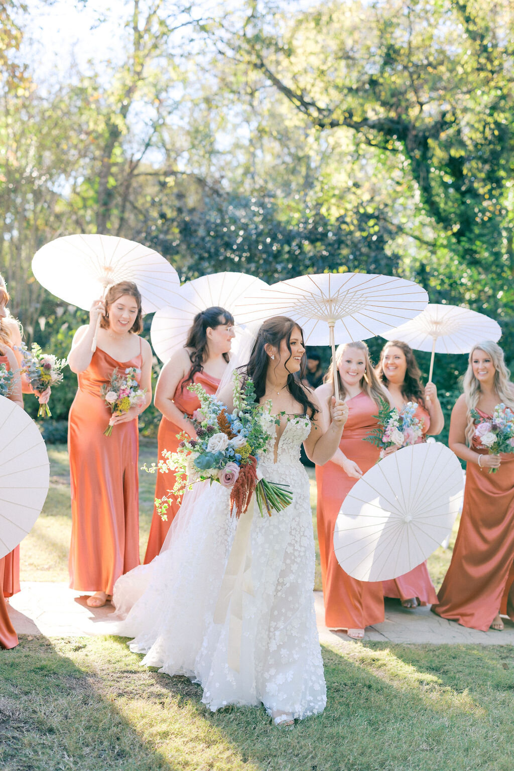 Outdooe summer wedding with bride and bridesmaids holding parisols