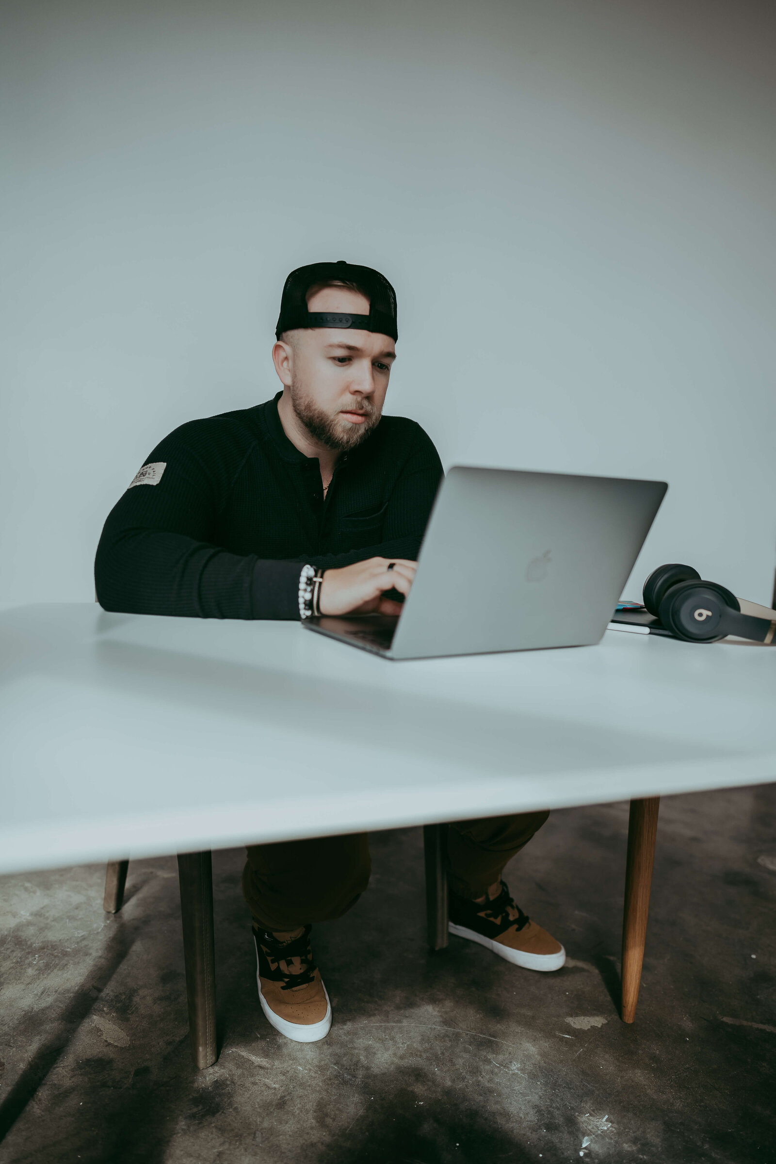 Amen sits at a white desk with his hat on backwards, working on his laptop during a personal branding session in Denver.