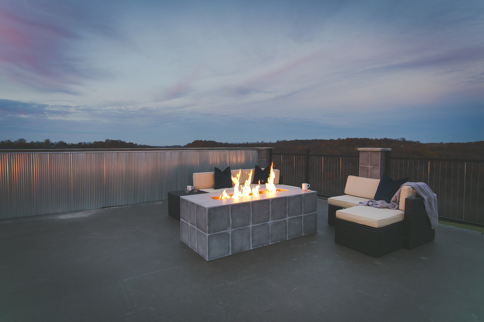 Modern Bnb rooftop design with custom cement gas fireplace. Industrial siding  and black metal railing surrounds the rooftop.