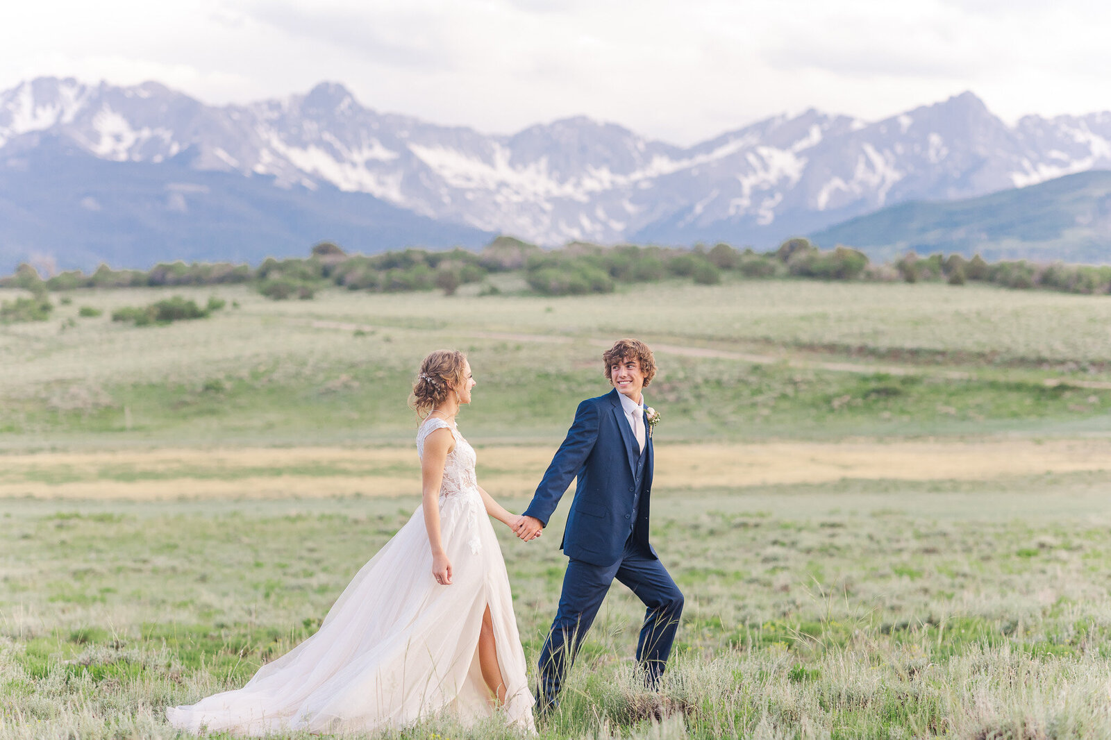 groom leads bride walking by the mountains