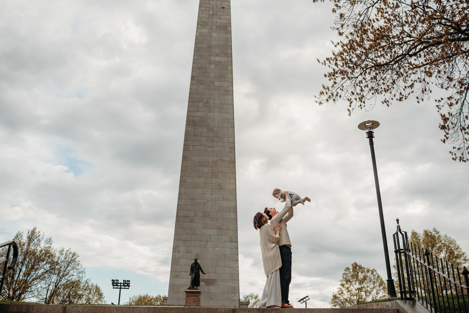 family holds little girl in air by bunker hill monument in charlestown during photoshoot