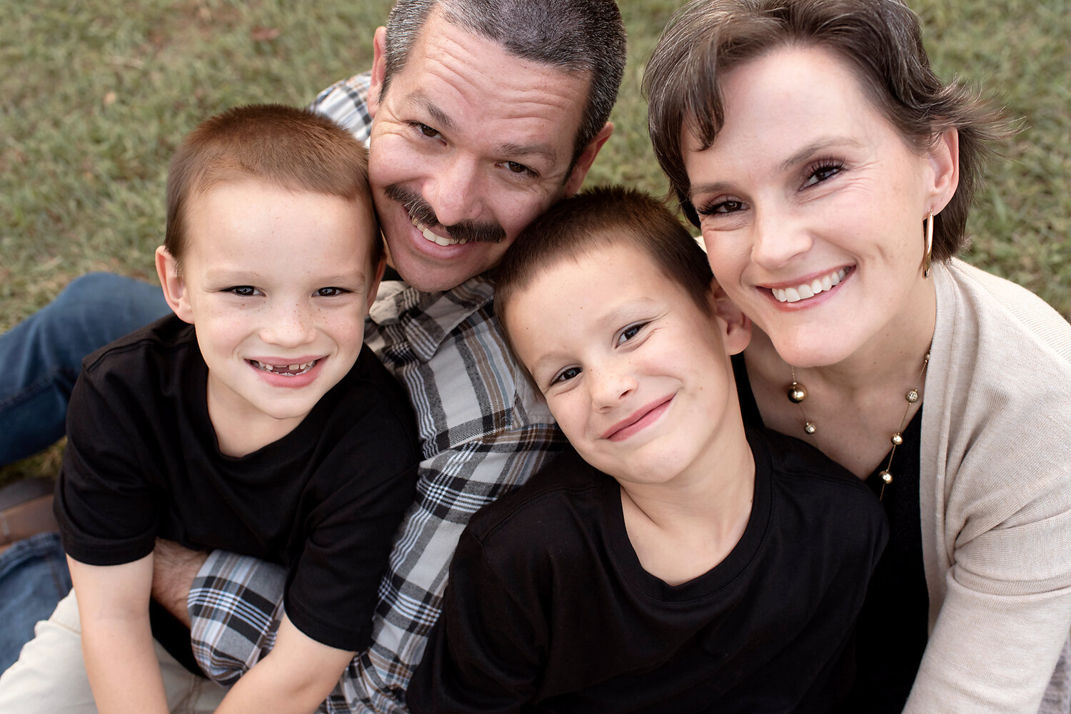 Parents with two young boys cuddling and smiling looking up at the camera.