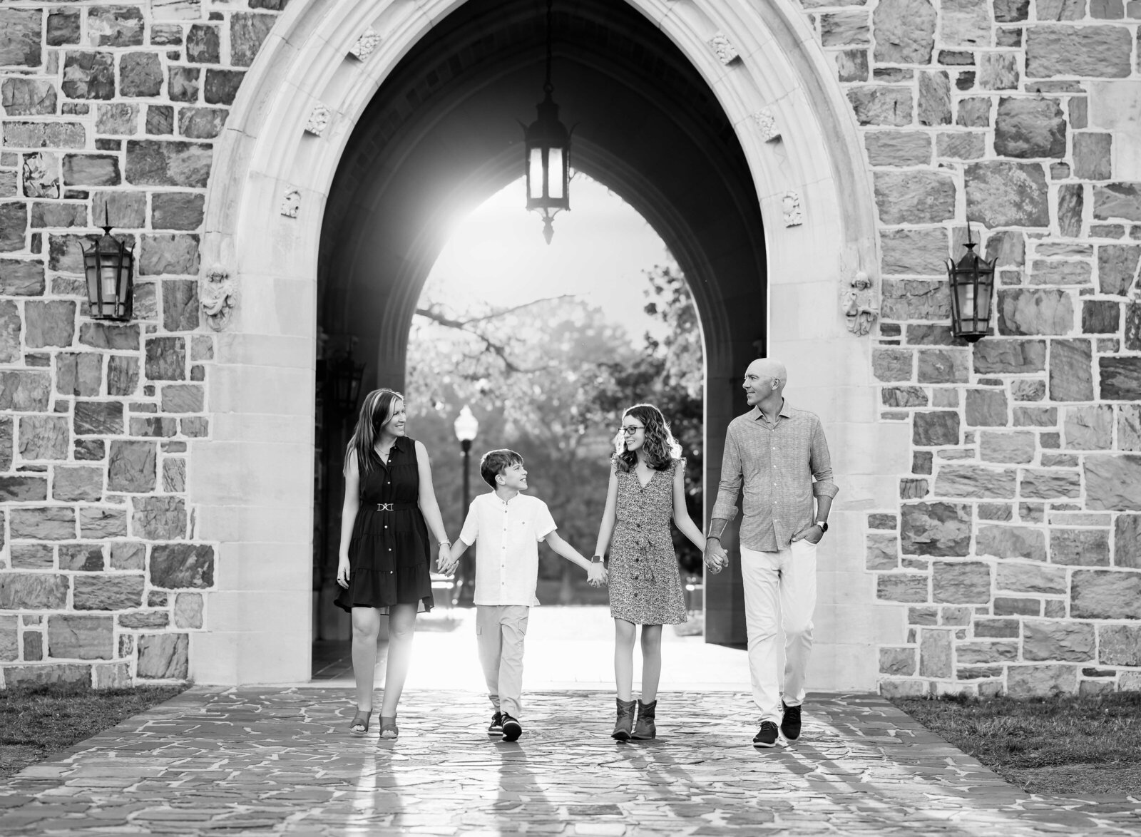 B&W family photo of Mom, dad and kids holding hands under Berry College arch structure. Family Photography by Jenni Nikki Photography- Atlanta Family Photographer.