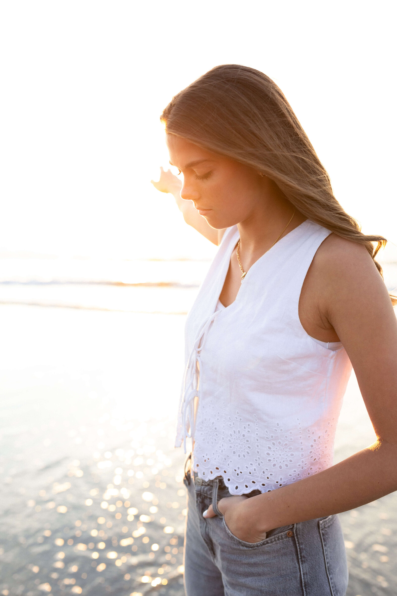 brunette high schooler posing on a beach wearing a white shirt