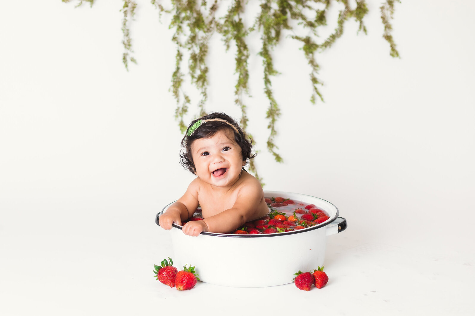 Milestone Photographer, a baby sits in a ceramic pot , full with floating strawberries