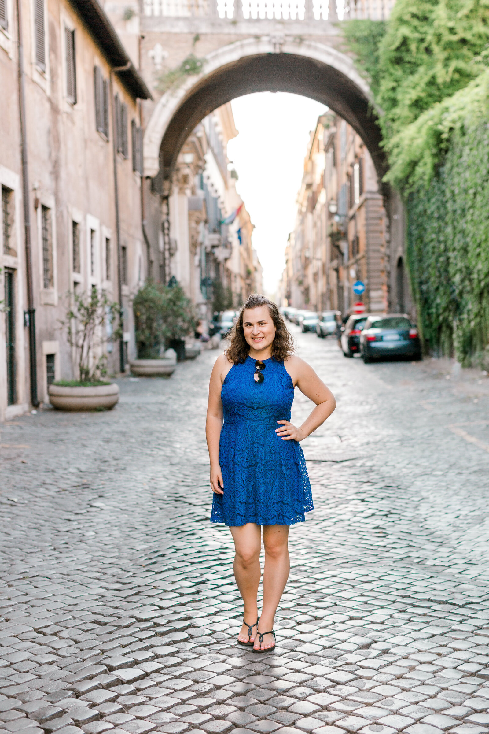 Woman standing along on a brick street with her hand on her hip.